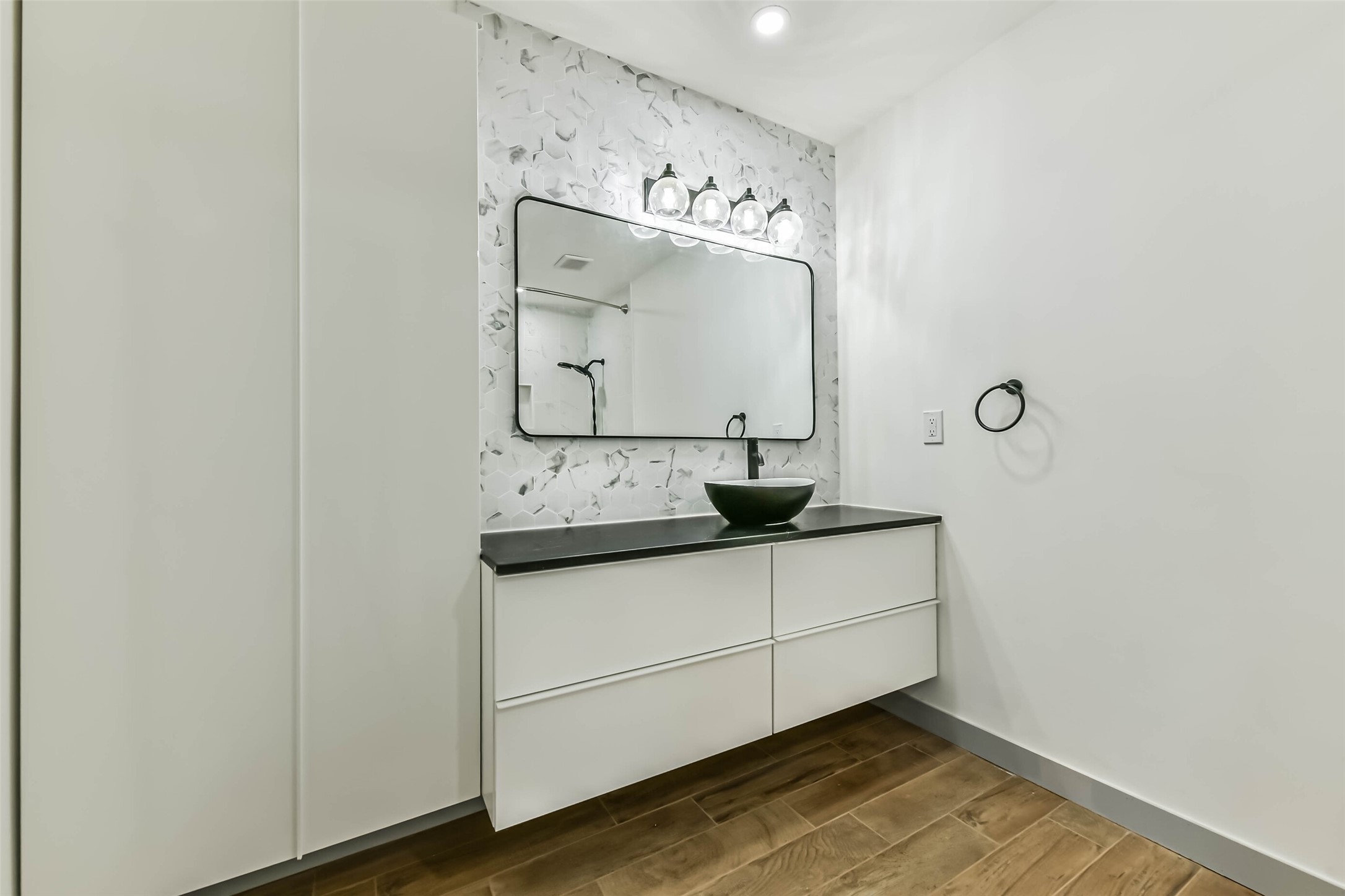 Bathroom features a modern design with a floating vanity, sink, and large mirror. The wall has a stylish tile accent, complemented by sleek lighting, and the wood-look flooring adds warmth to the space.