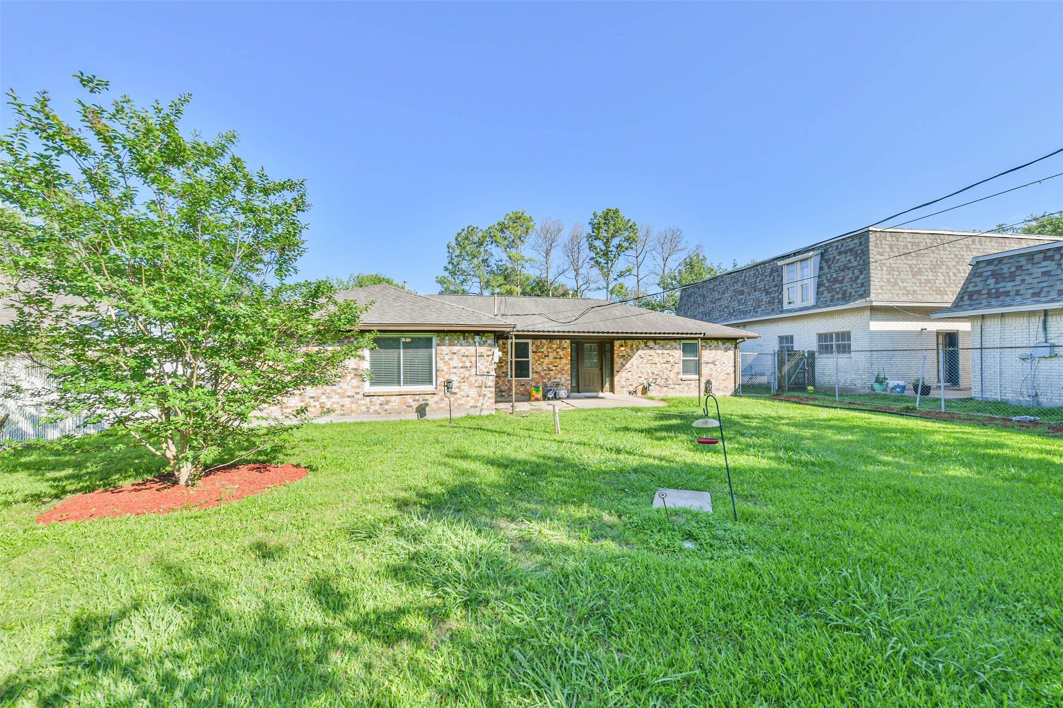 Backyard with well-maintained grass. The house features a stone facade, a covered patio area, and ample space for outdoor activities.