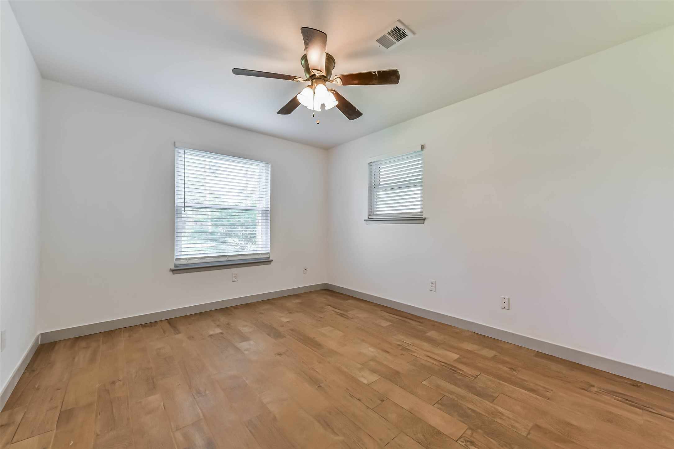 Bedroom features hardwood floors, neutral walls, and a ceiling fan. Two windows provide natural light.