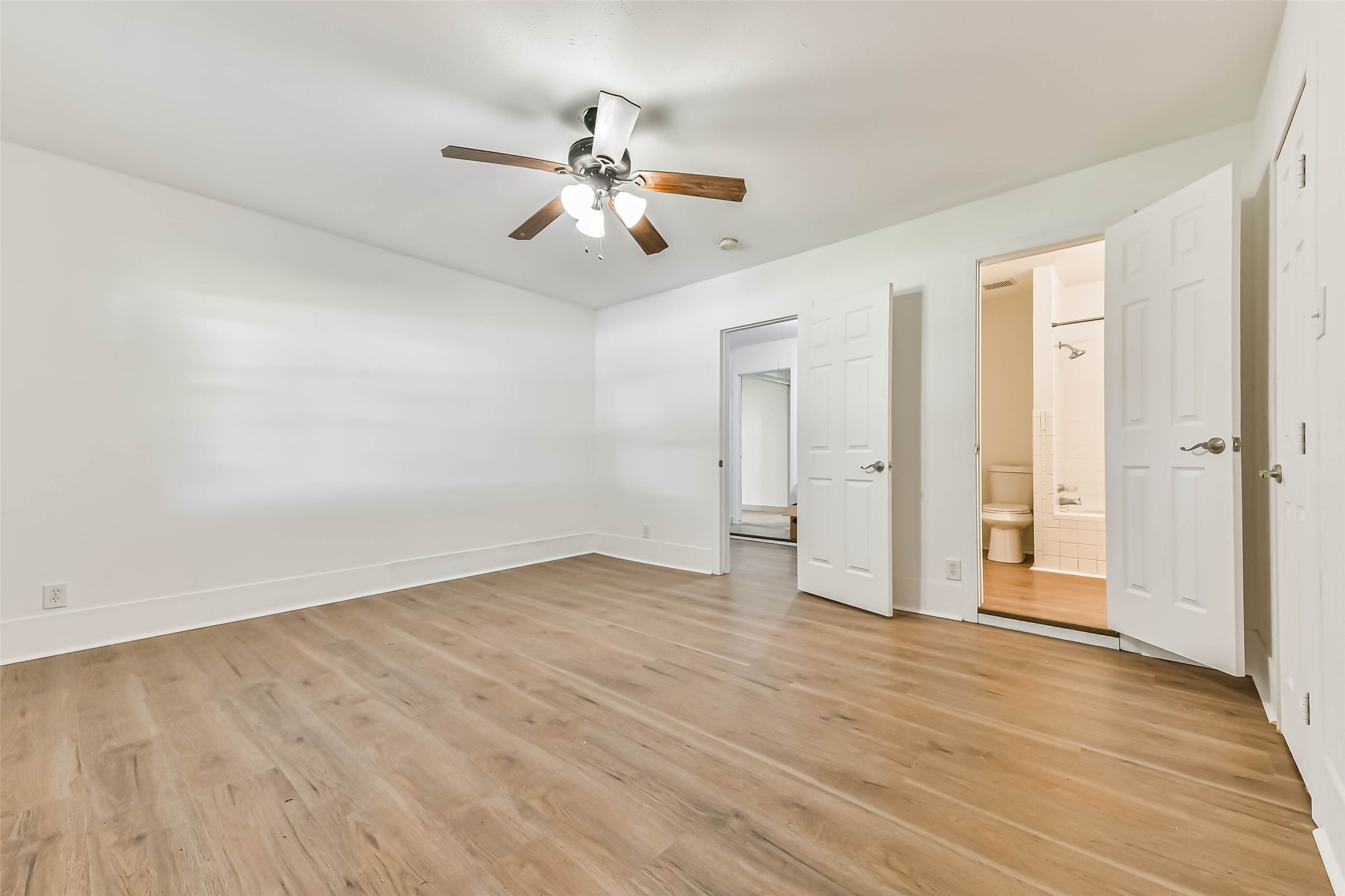 Bedroom with wood flooring, a ceiling fan, and neutral walls. It features access to an en-suite bathroom.