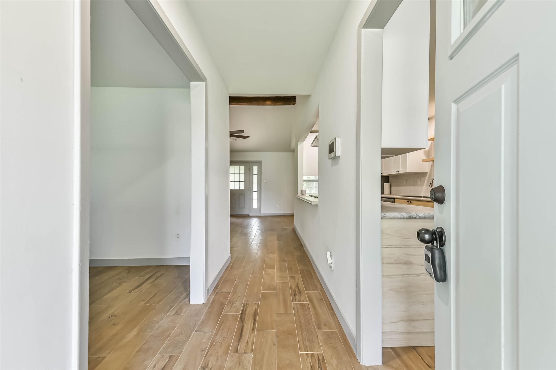 Entryway with wood-style flooring. The hallway leads to the living area and a glimpse of the kitchen, featuring modern cabinetry. A well-lit and welcoming space.