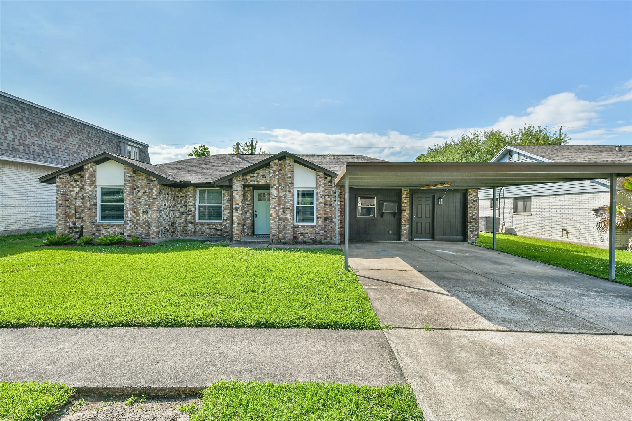 Single-story brick home with a well-maintained front lawn and a covered carport. It features a simple exterior design with a welcoming front entrance and a driveway.