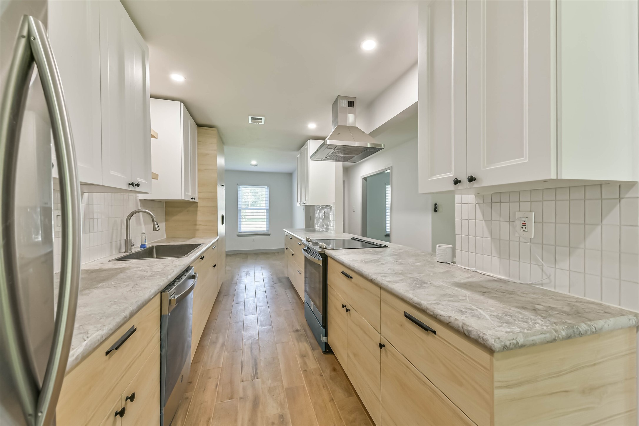 Kitchen features a modern design with light wood cabinetry, marble countertops, and stainless steel appliances. It has a sleek, bright look with white tile backsplash, ample storage, and recessed lighting.