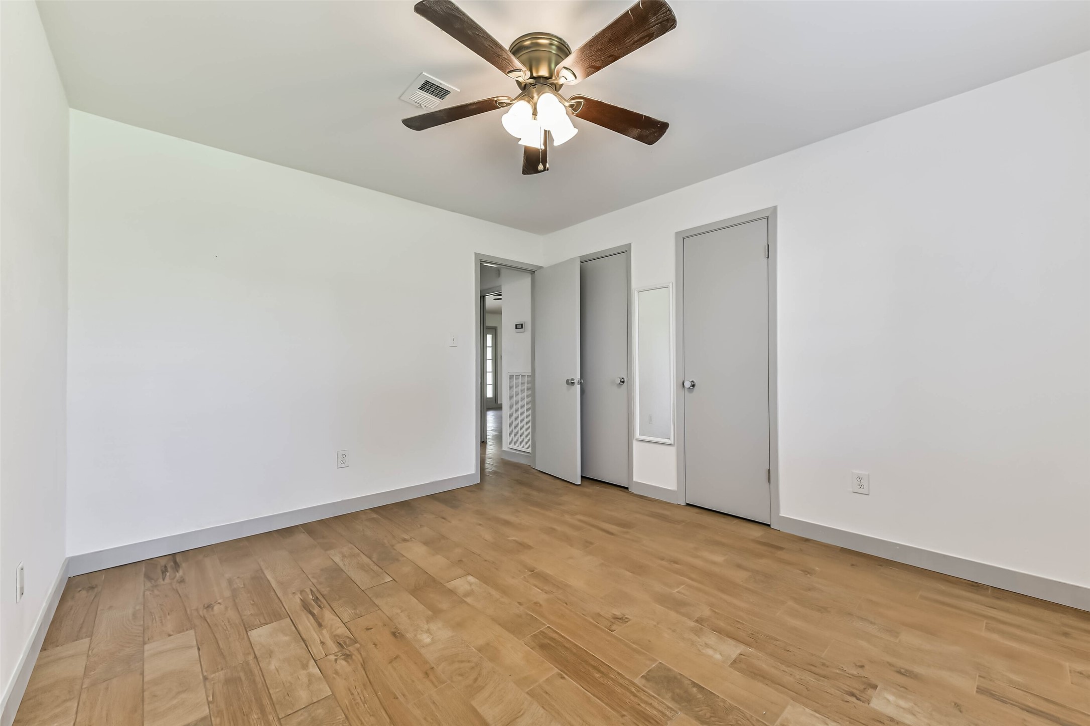 A spacious room with hardwood floors, a ceiling fan, and two doors.