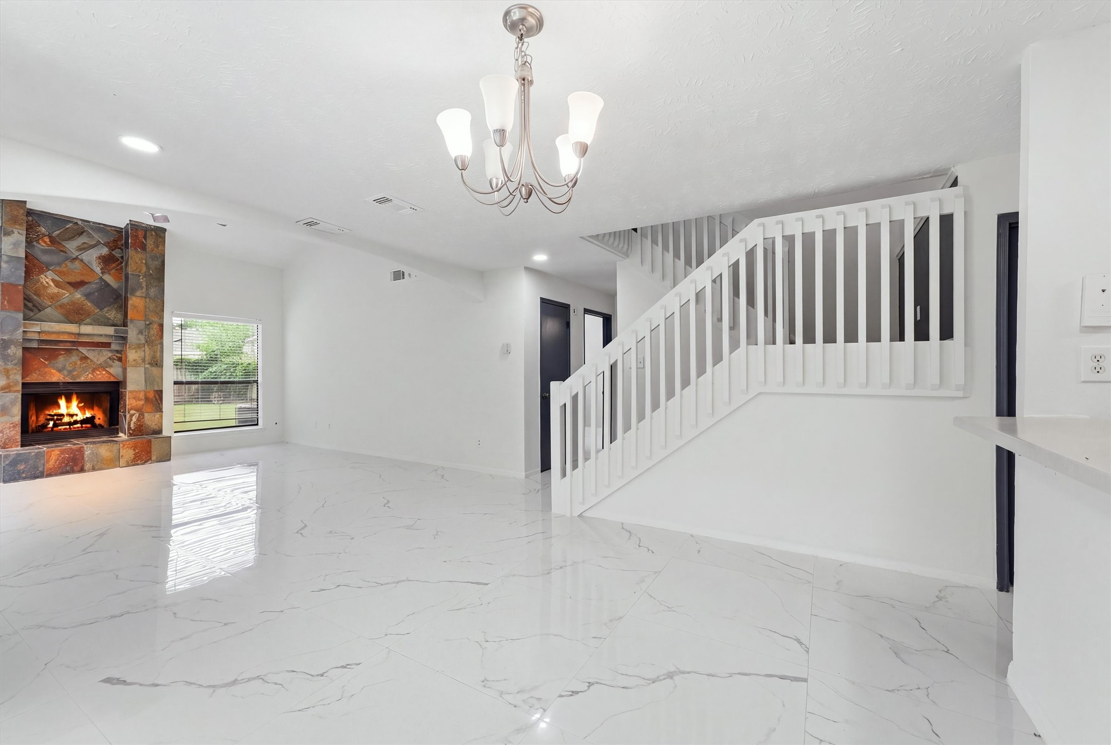 Dining area sits beside the kitchen beneath a chandelier, surrounded by three windows and glossy marble-look tile flooring.