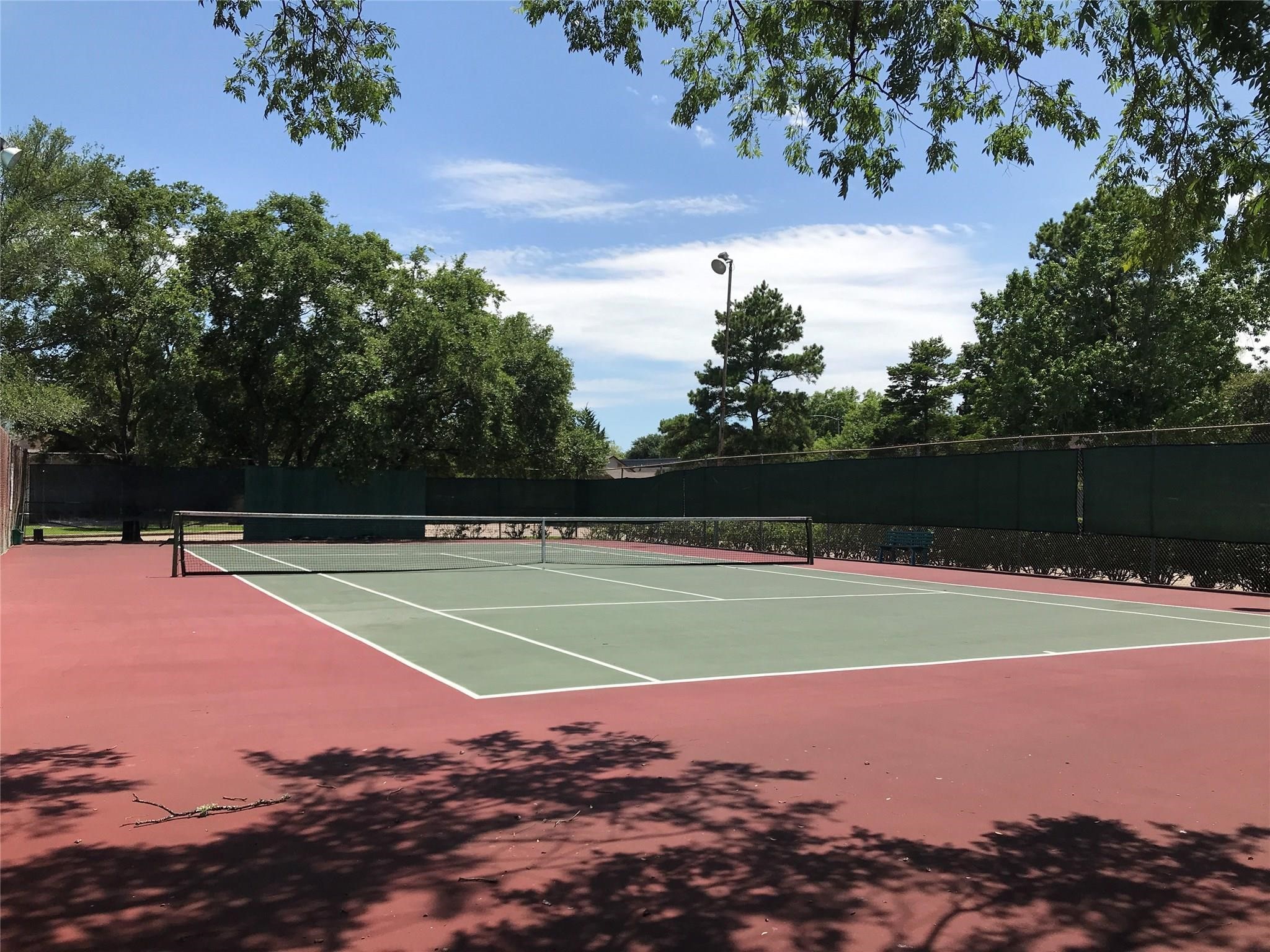 Westpark Village Tennis court is surrounded by fencing and mature trees, providing an outdoor space for recreational activities.
