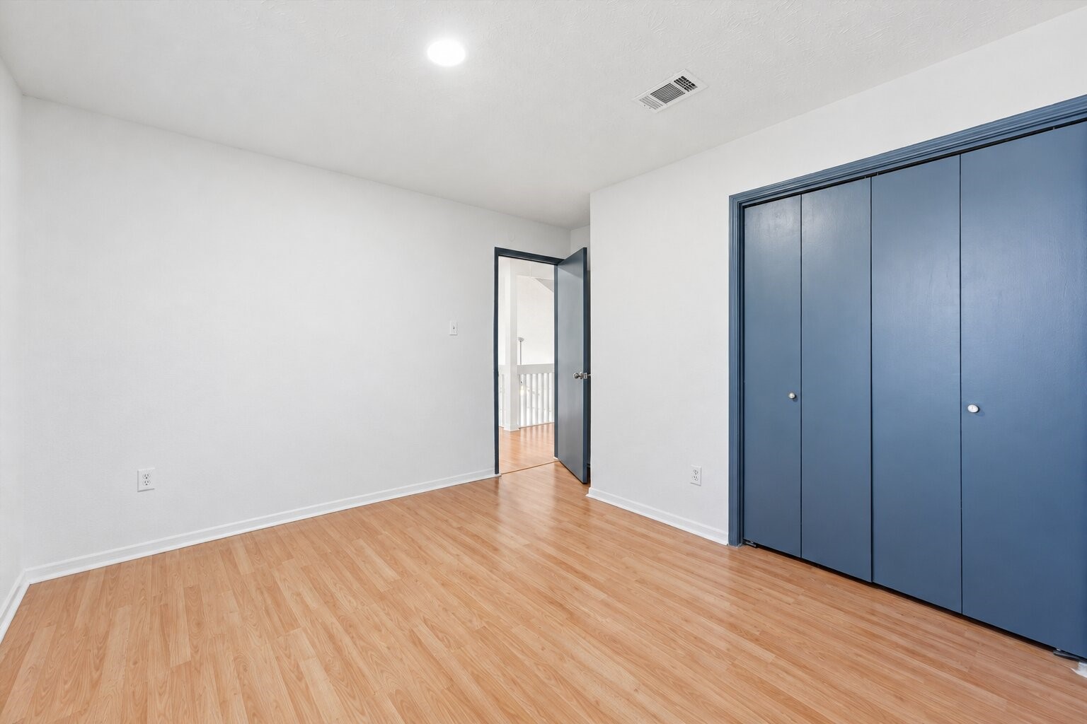 Secondary bedroom includes a wide double-door closet, wood-look flooring, and a doorway leading toward the hallway.