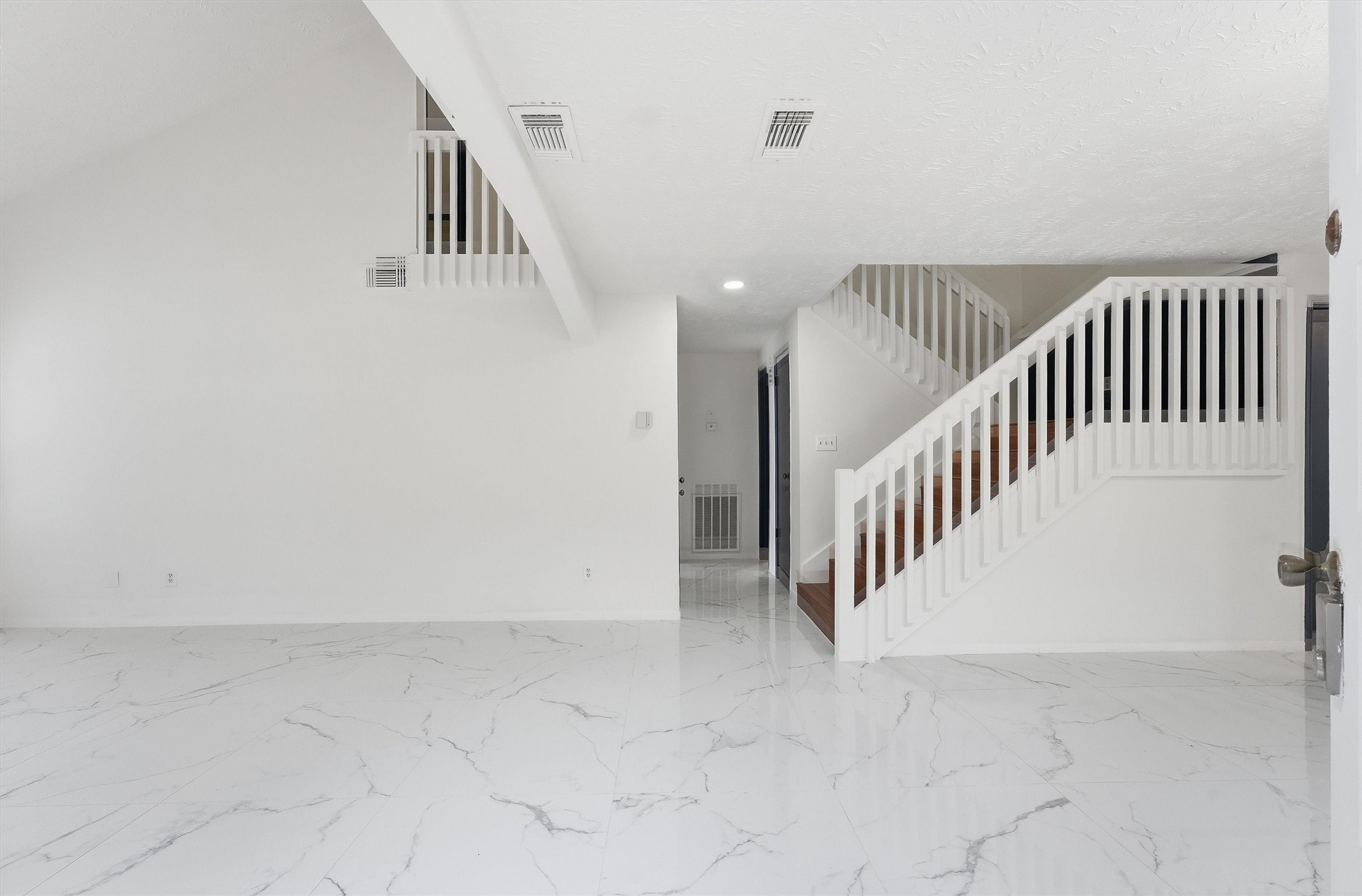Entryway opens to glossy marble-look tile flooring and a staircase with white railings leading to the upper level. Entryway opens to glossy marble-look tile flooring and a staircase with white railings leading to the upper level.