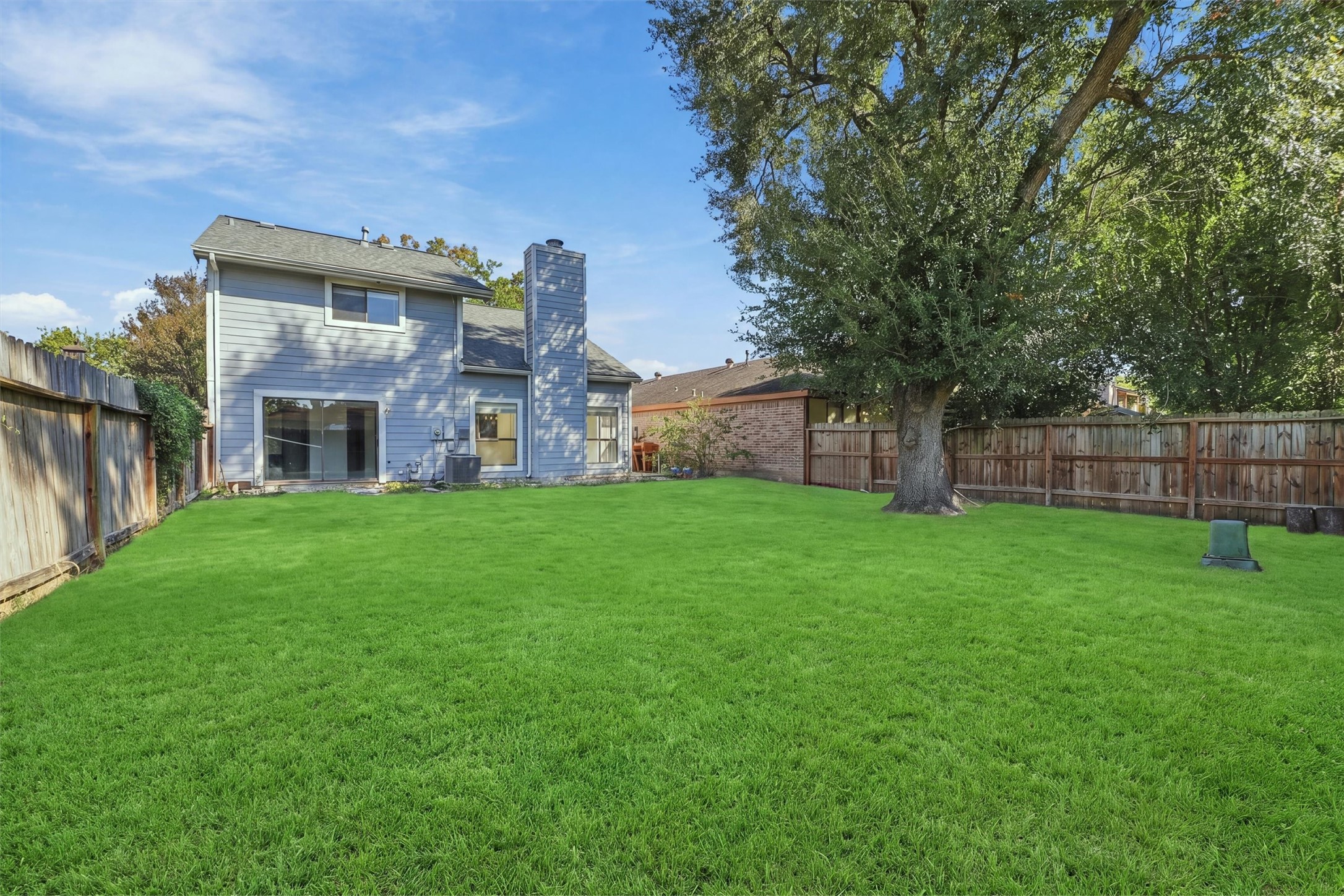 Backyard welcomes outdoor activities on a spacious green lawn surrounded by a wood fence and mature trees.