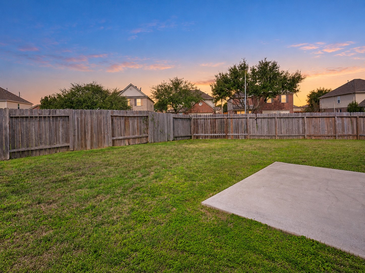 Spacious fenced backyard with an open lawn and concrete patio, offering flexibility for outdoor entertaining and recreation.