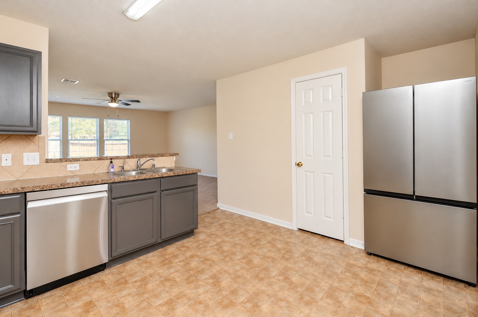 Additional kitchen view showcasing the stainless steel refrigerator, dishwasher, ample cabinetry and open connection to the family room.