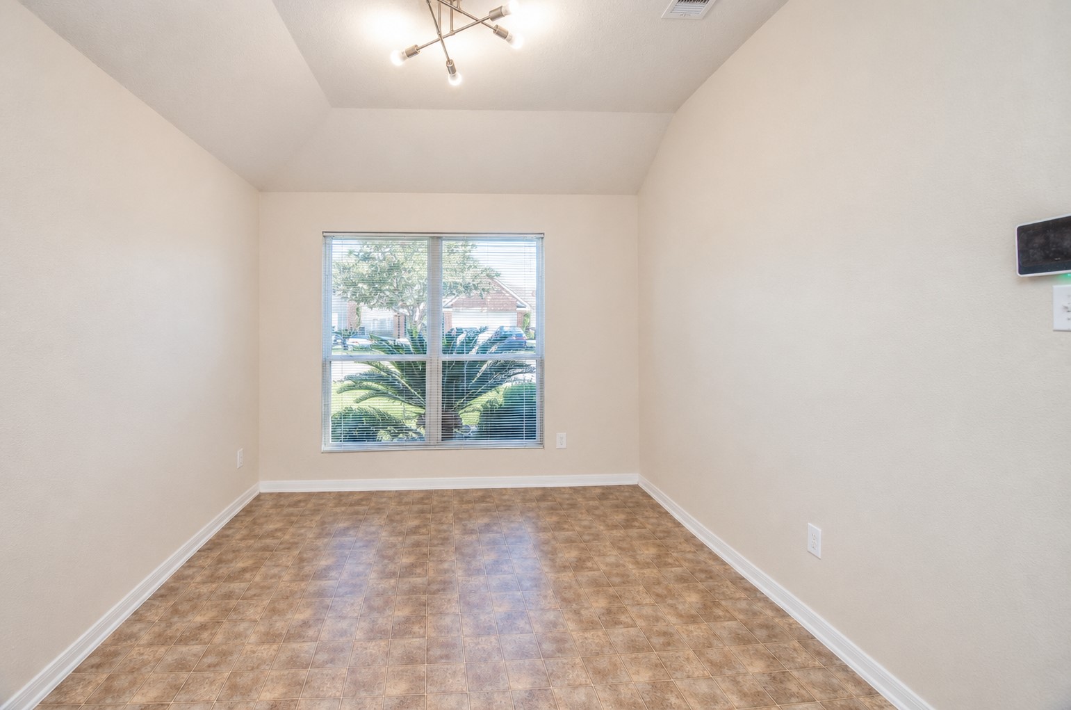 Formal dining room with a vaulted ceiling, decorative light fixture and large window overlooking the front landscaping.