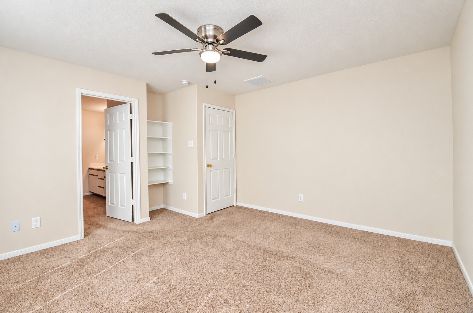 Additional view of the first-floor primary suite highlighting the generous floor space, private bathroom entrance and built-in shelving.