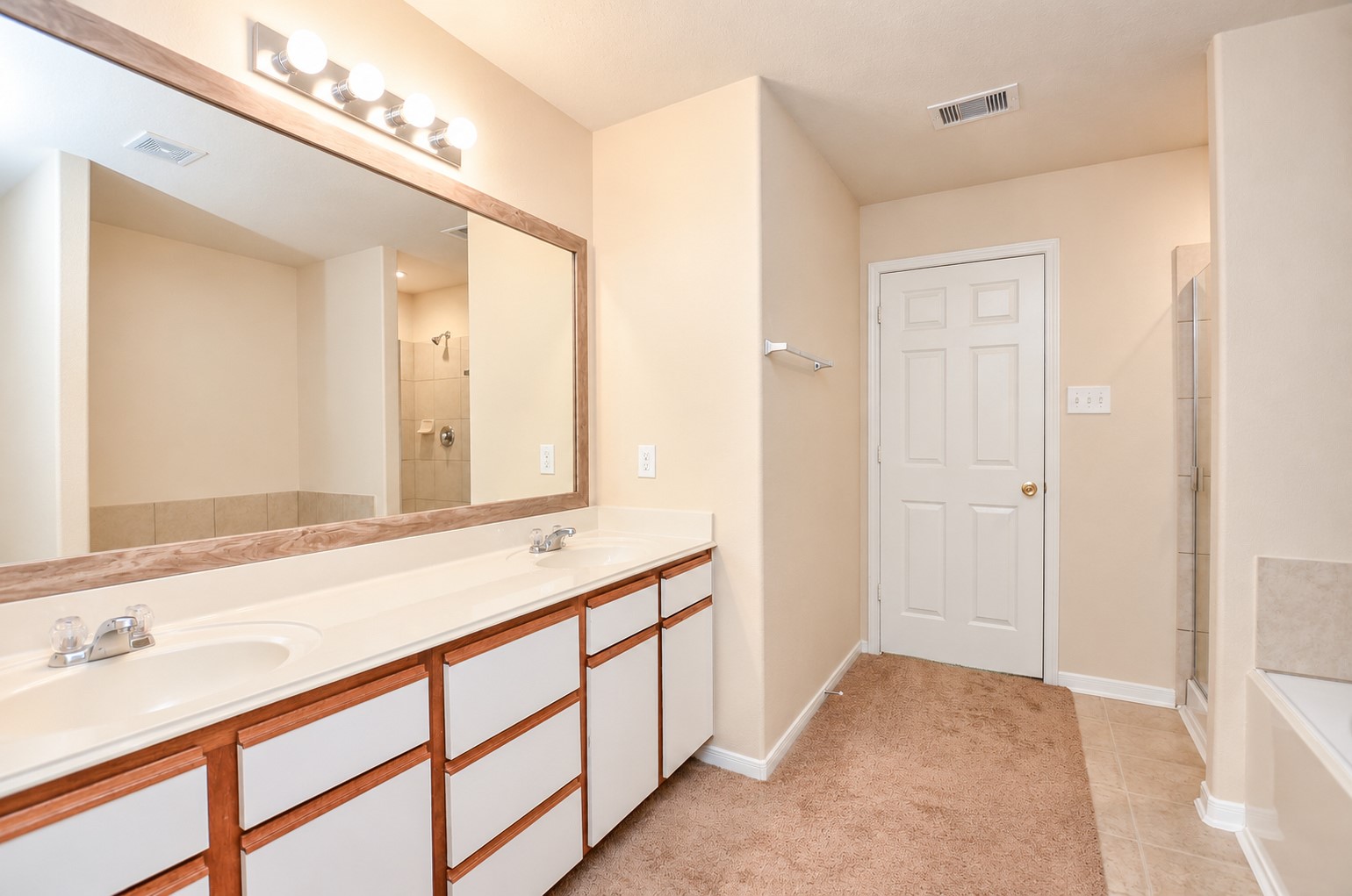 Spacious primary bathroom with an extended dual-sink vanity, large framed mirror and separate tub and shower.