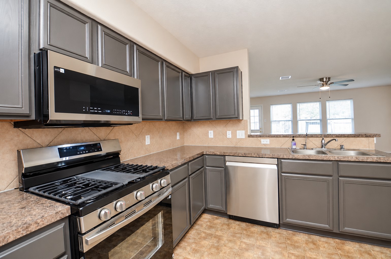 Closer view of the kitchen showcasing the stainless steel gas range, built-in microwave, dishwasher and attractive gray cabinetry.