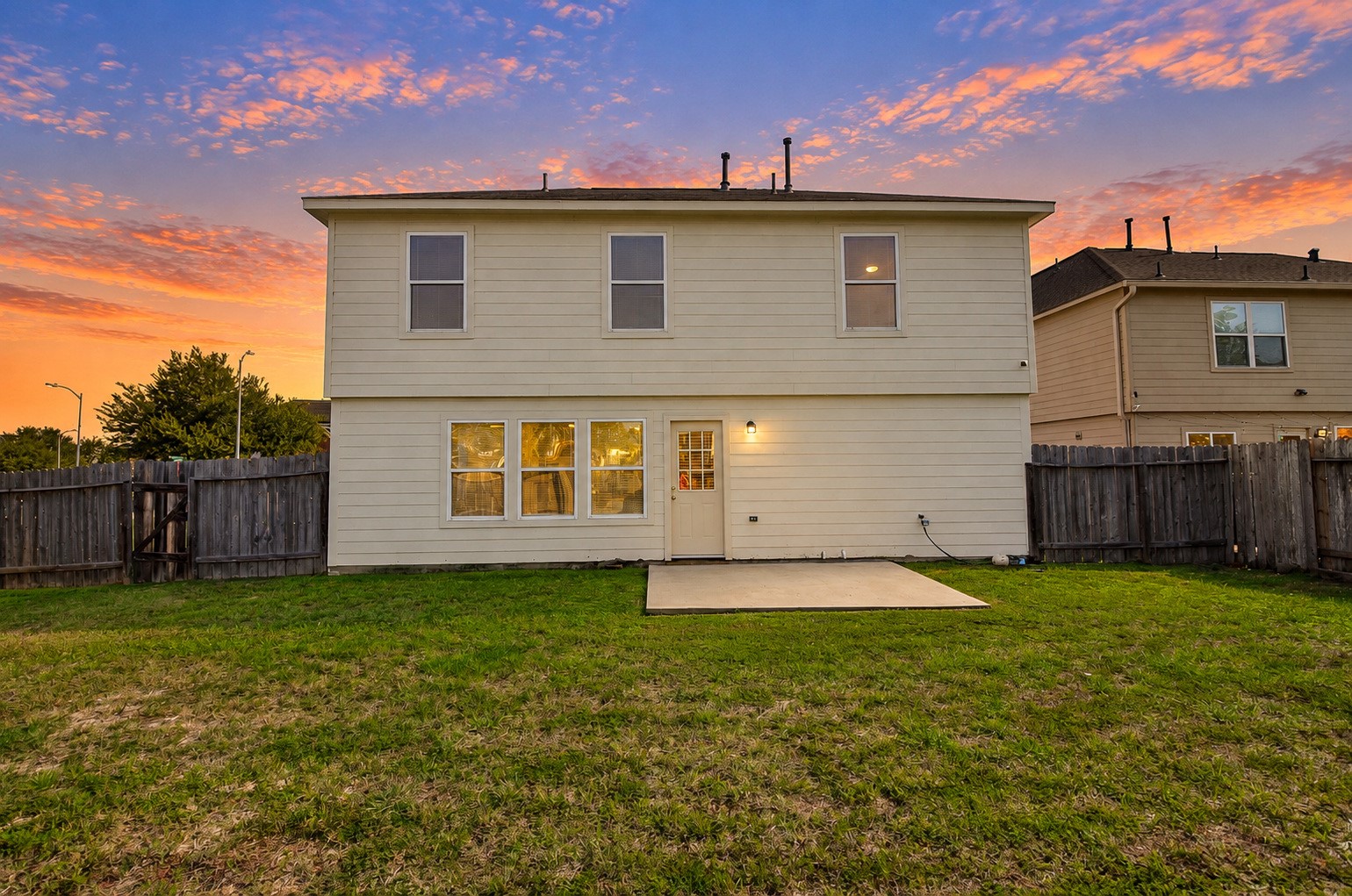 Full rear elevation showcasing the two-story home, multiple windows, concrete patio and spacious fenced backyard.