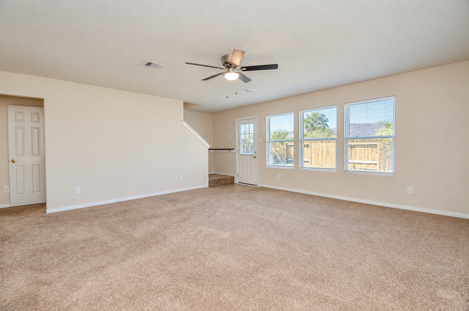 Spacious family room featuring a ceiling fan, neutral carpeting and abundant natural light from multiple windows.