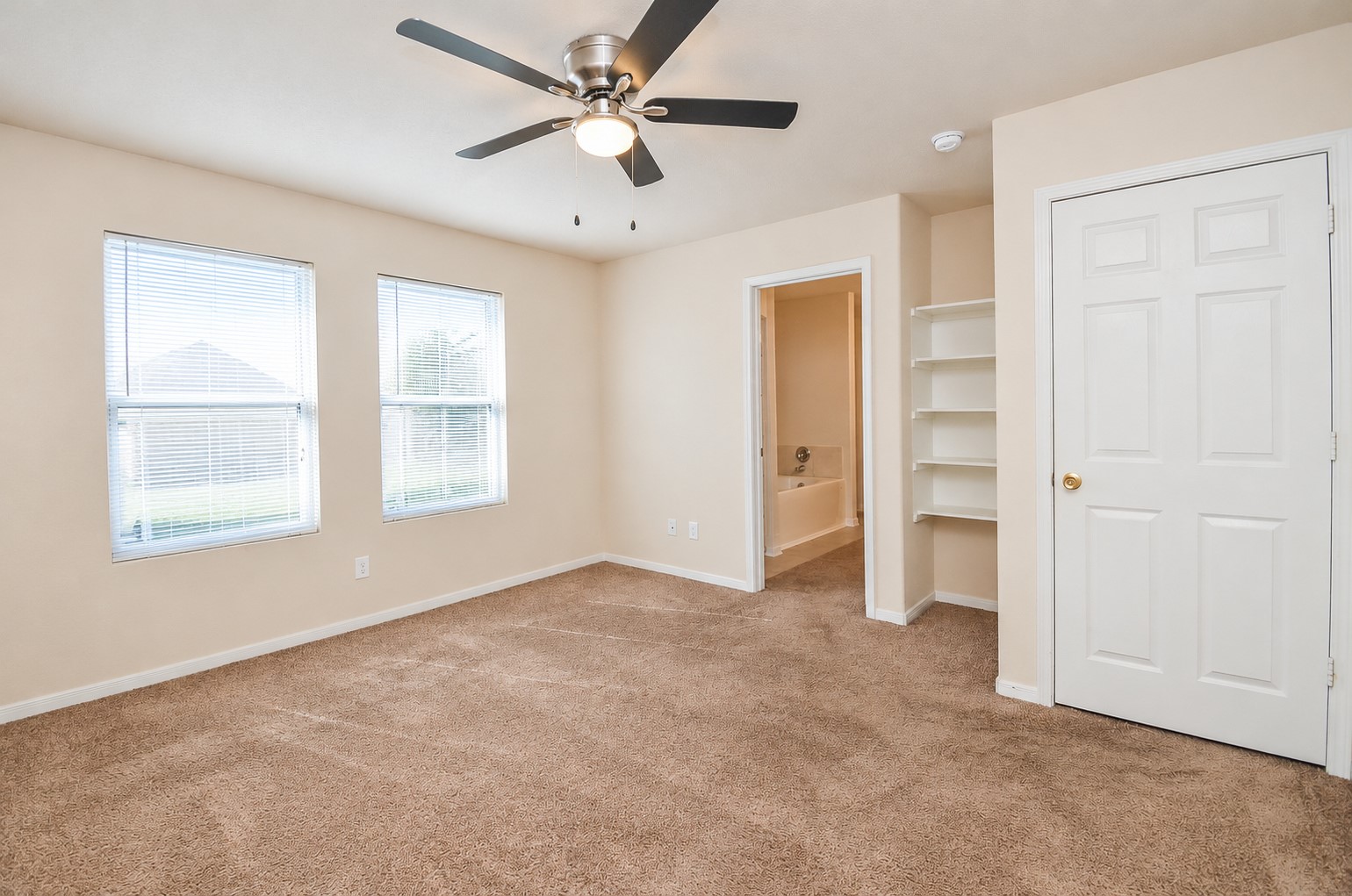 Spacious first-floor primary bedroom with two windows, a ceiling fan and convenient access to the private bathroom and walk-in closet.
