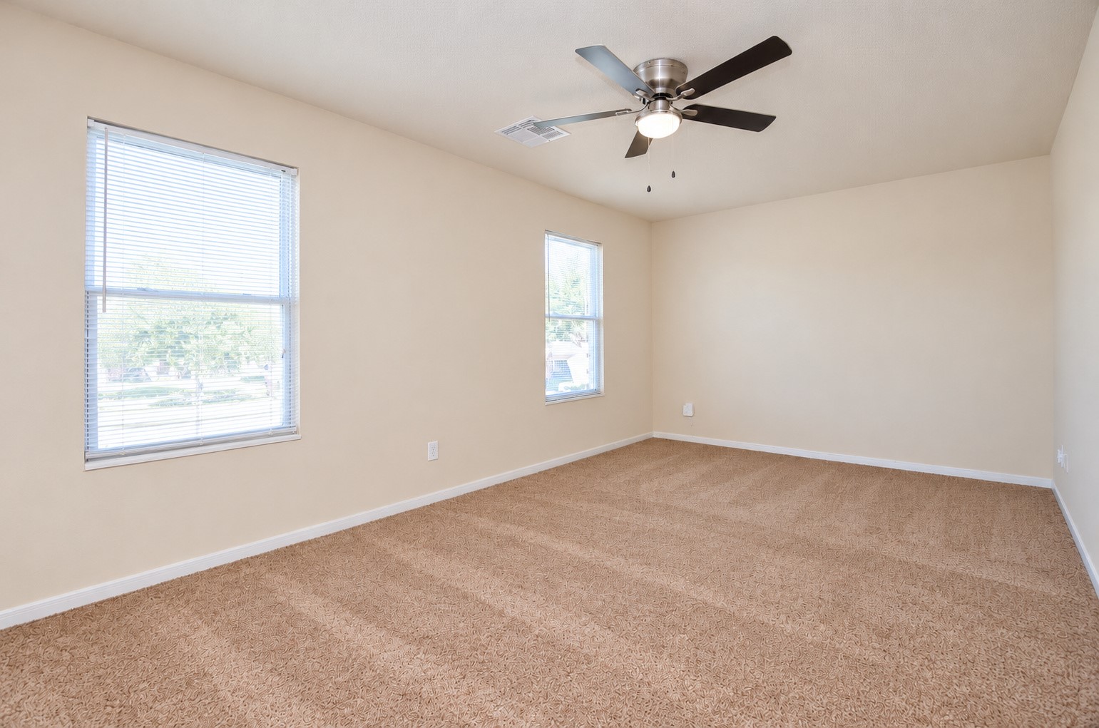 Spacious upstairs game room featuring neutral carpeting, a ceiling fan and windows providing natural light.