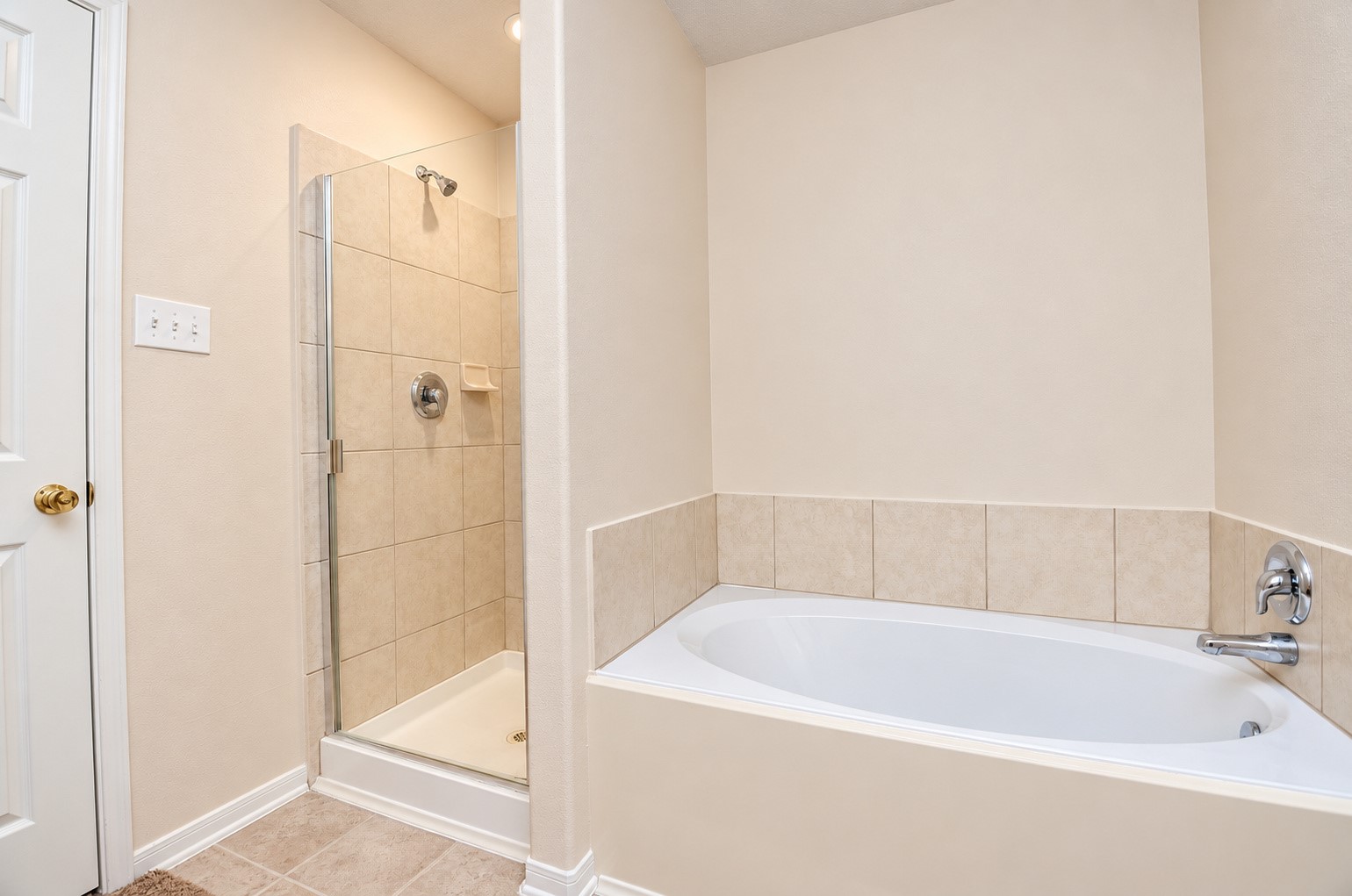 First-floor primary bathroom featuring a soaking tub, separate glass-enclosed shower and neutral tile finishes.