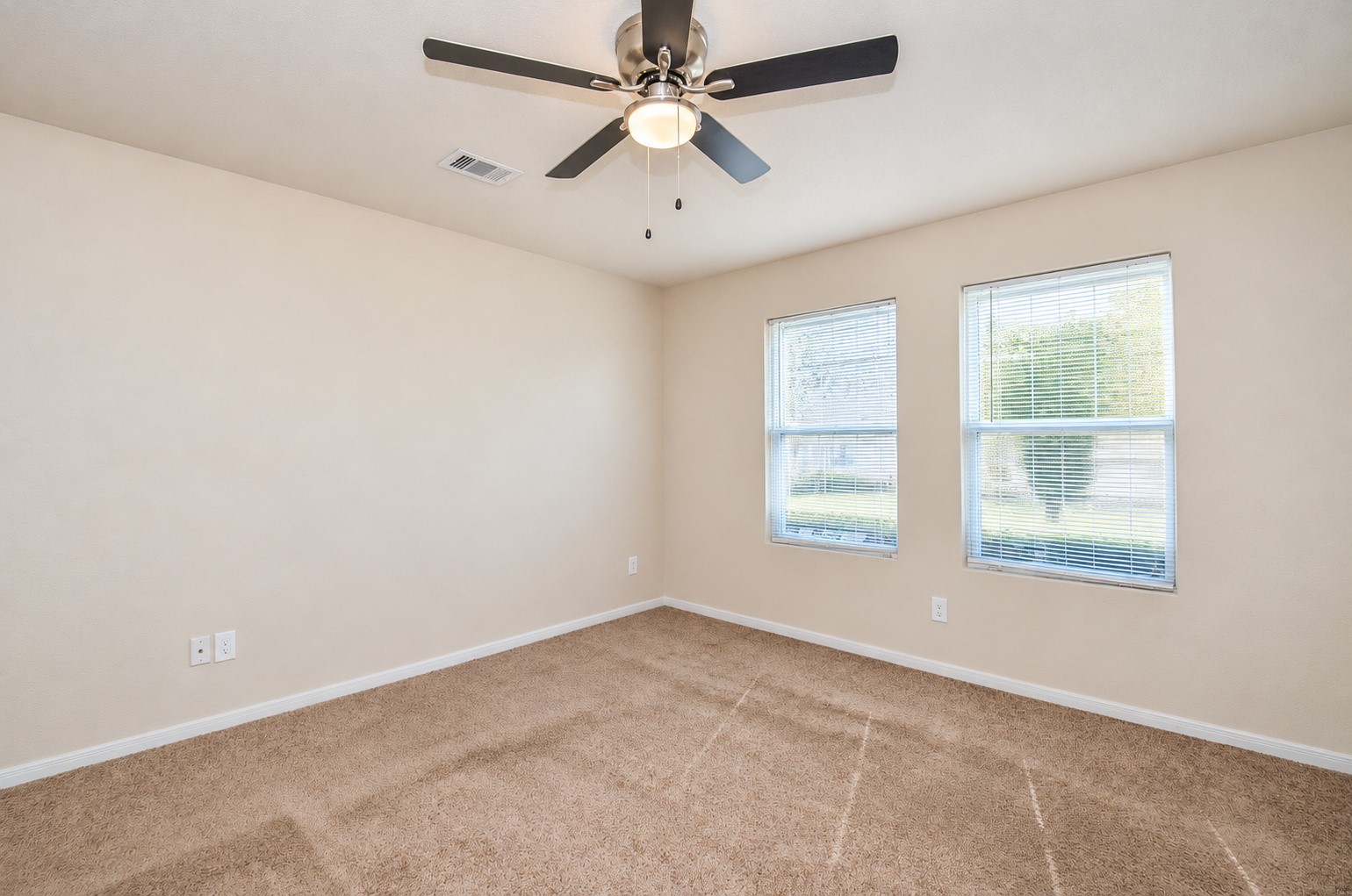 First-floor primary bedroom featuring neutral carpeting, a ceiling fan and two windows providing abundant natural light.