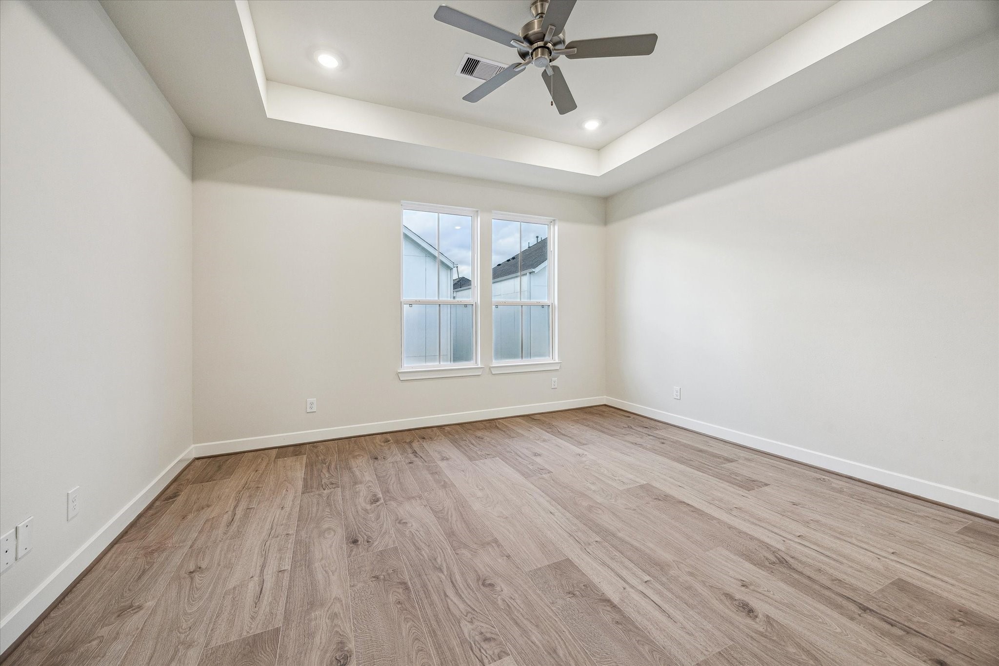 Large primary bedroom featuring a tray ceiling, recessed lighting, ceiling fan, and large windows for natural light.