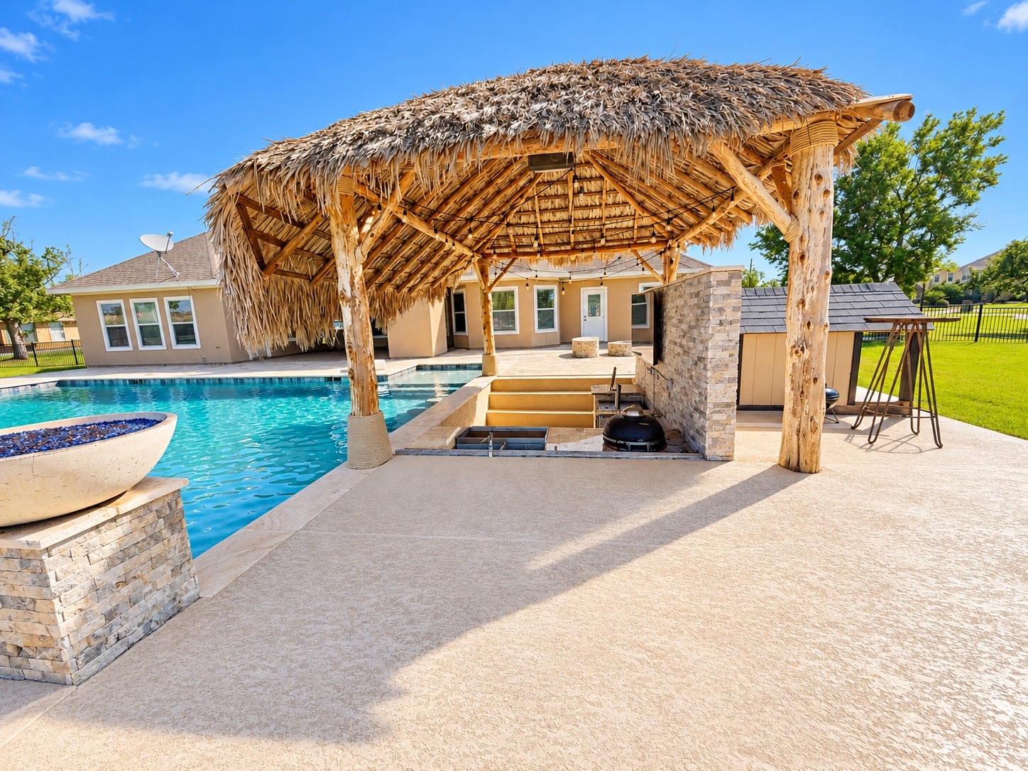 Luxurious outdoor oasis featuring a sparkling pool, poolside cabana with a thatched roof, and built-in entertainment area, perfect for relaxation and entertaining.