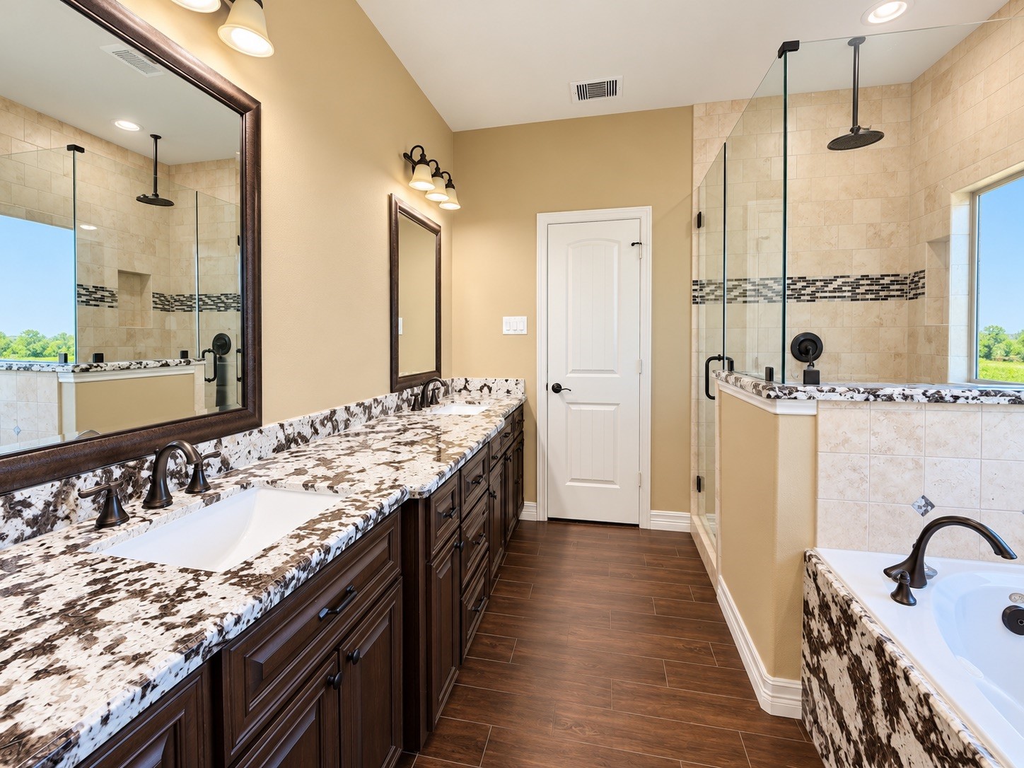 Elegant bathroom featuring dual sinks with striking granite countertops, a spacious glass-enclosed shower, and a luxurious soaking tub, all enhanced by warm wood cabinetry and modern fixtures.