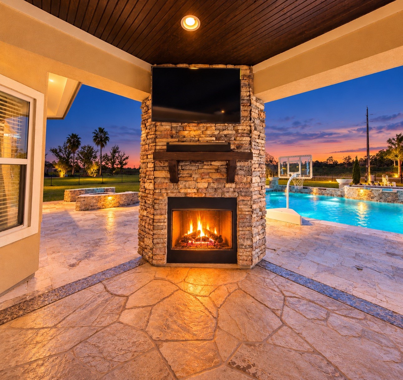 Experience outdoor luxury with a stunning stone fireplace and entertainment area, overlooking a sparkling pool and serene sunset views.