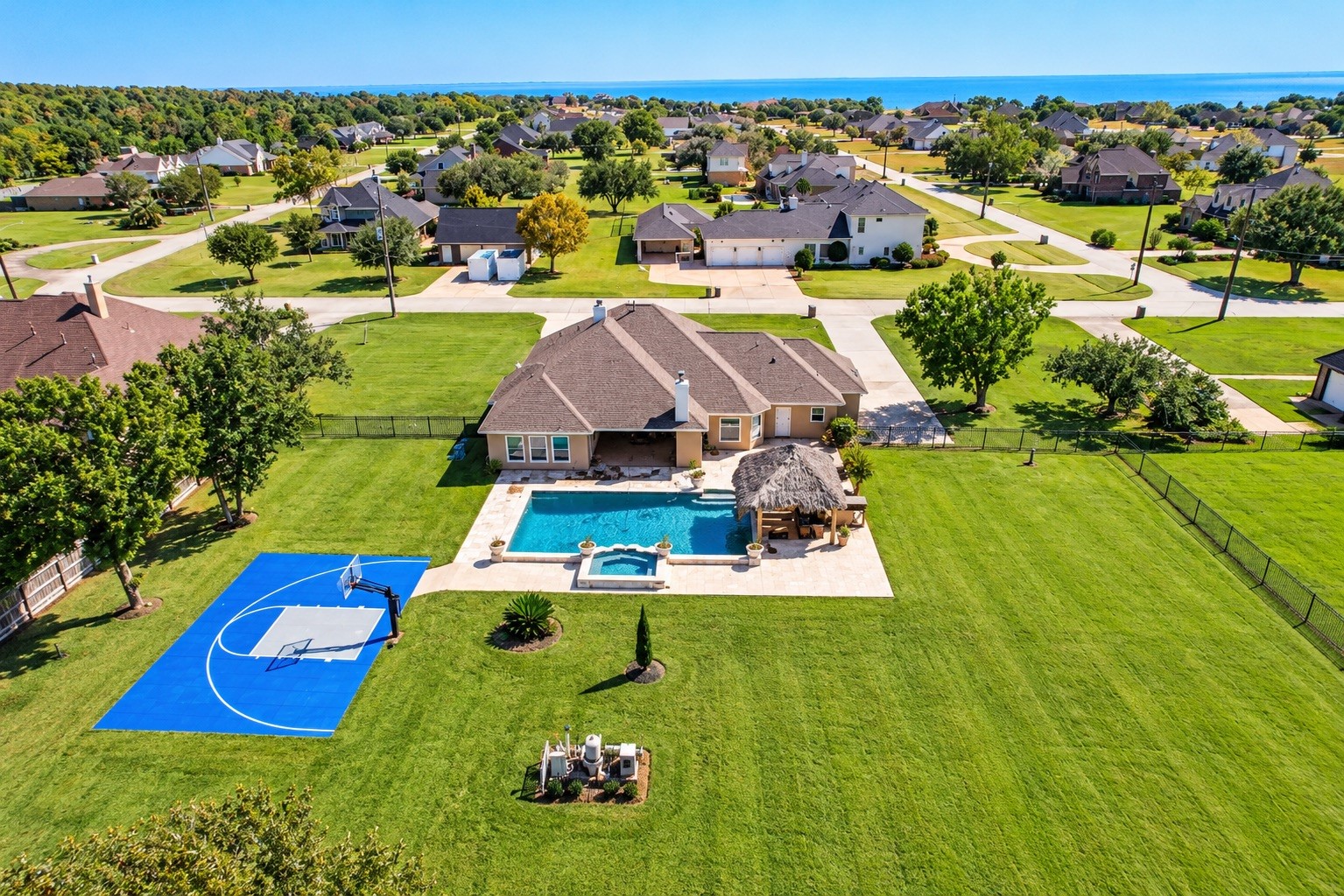 Expansive property featuring a beautiful backyard with a sparkling pool, thatched cabana, and a private basketball court, all set in a serene neighborhood with spacious green lawns.