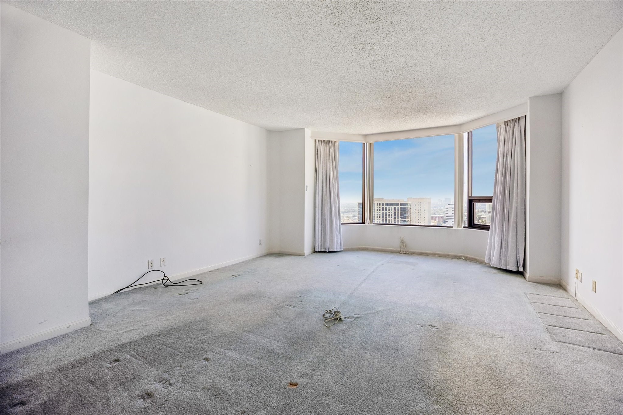 Bay windows frame city views, with neutral walls and carpeted flooring providing a soft backdrop. Open floor space allows you to shape a comfortable den with your own colors and personal touches.