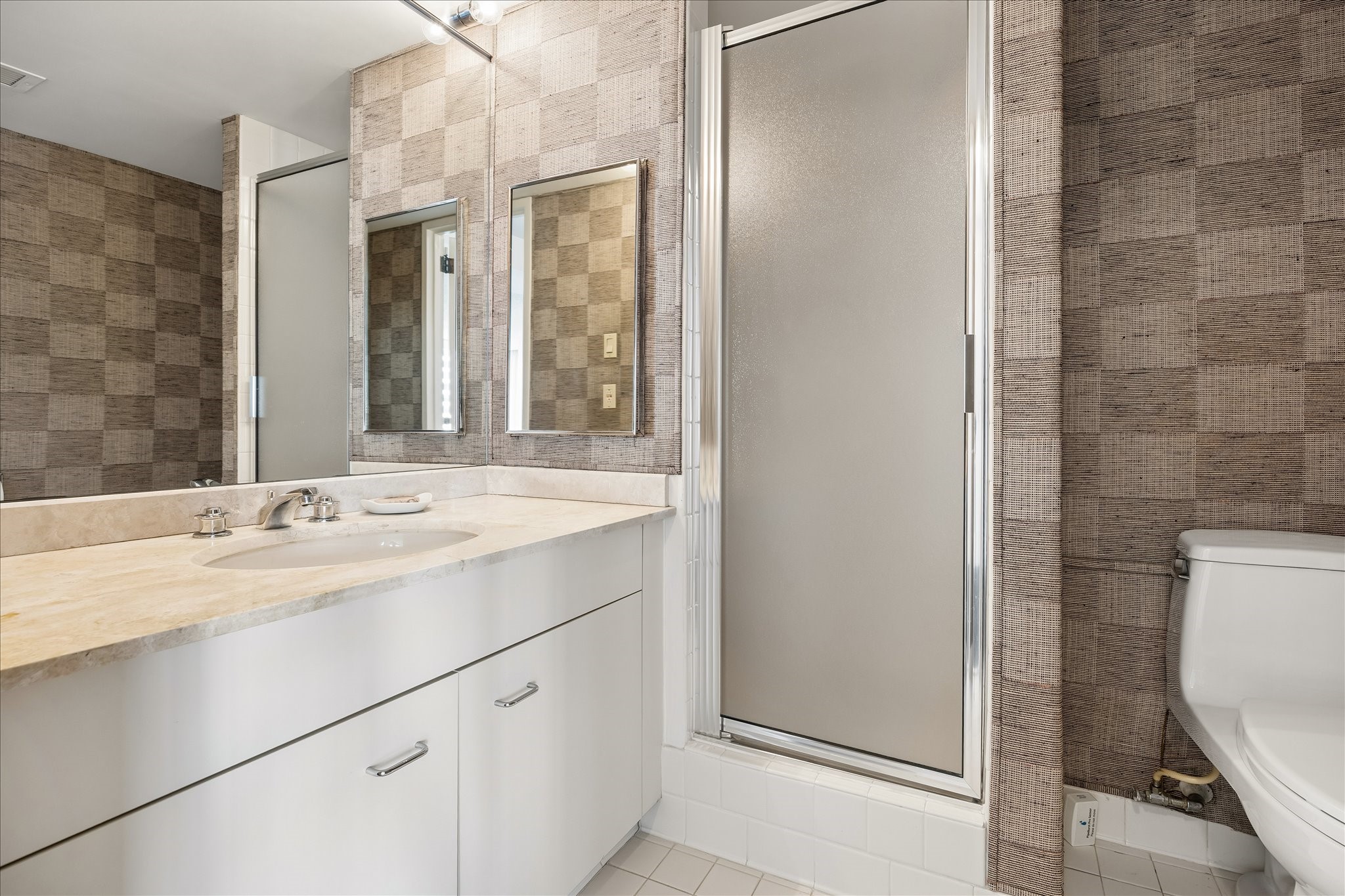 Wide vanity counters and drawers provide practical space for daily routines and bathroom storage. A mirrored wall and frosted glass shower enclosure complete this bath, one of 3 in the residence.