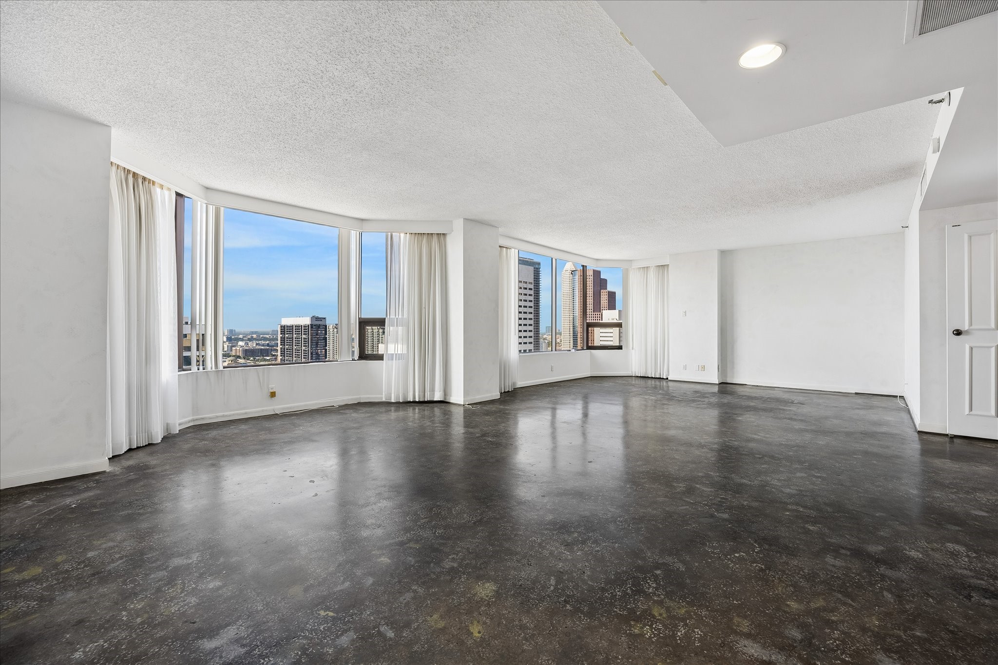 Broad window bays frame downtown views and fill the living area with natural light. Dark concrete flooring and neutral walls create a blank slate for your personal touches, with open space to shape around the way you live.