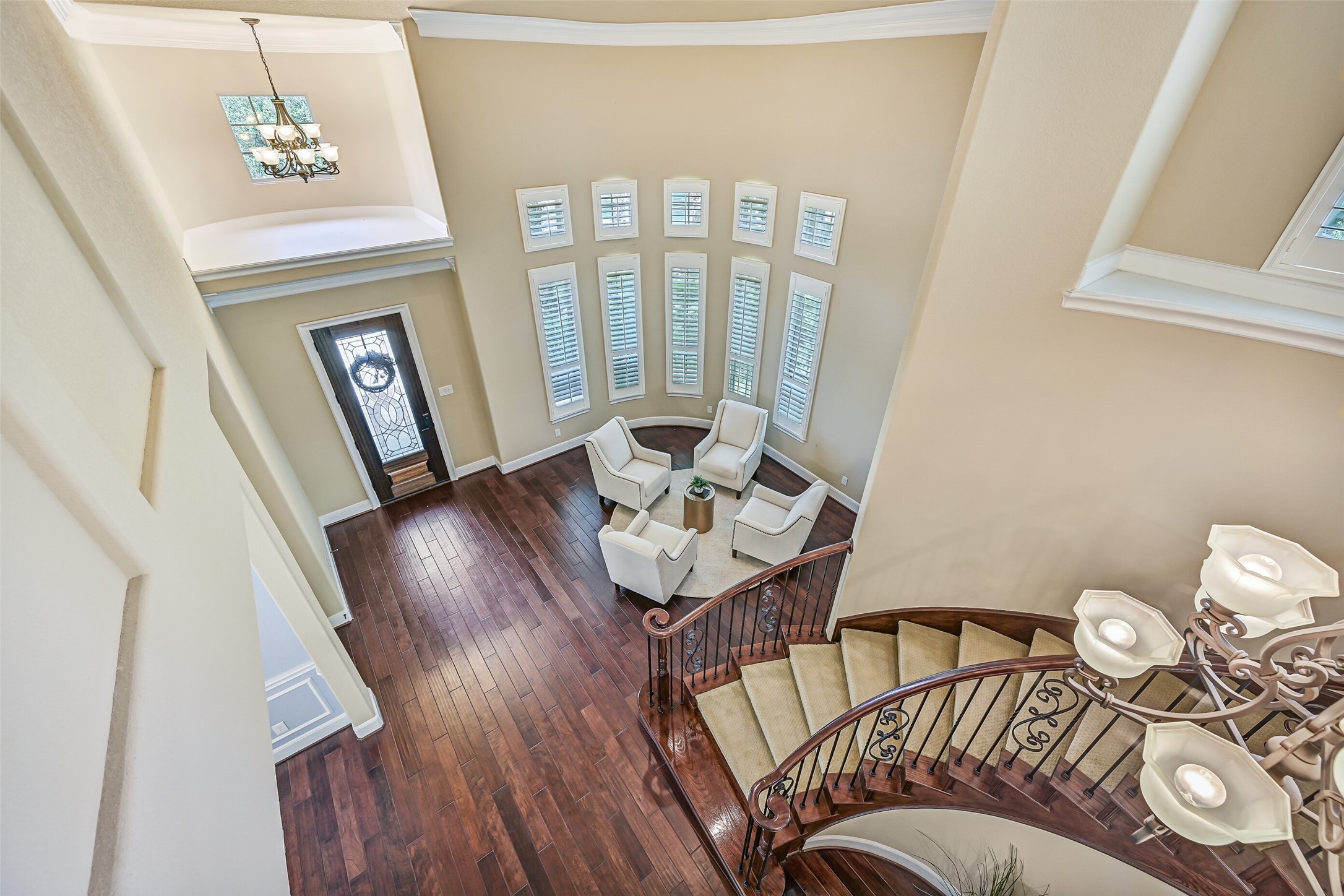 A dramatic birds-eye view showcases the homes impressive two-story entry, sweeping curved staircase with wrought iron balusters, rich wood flooring, and a wall of towering windows that flood the foyer with natural light.