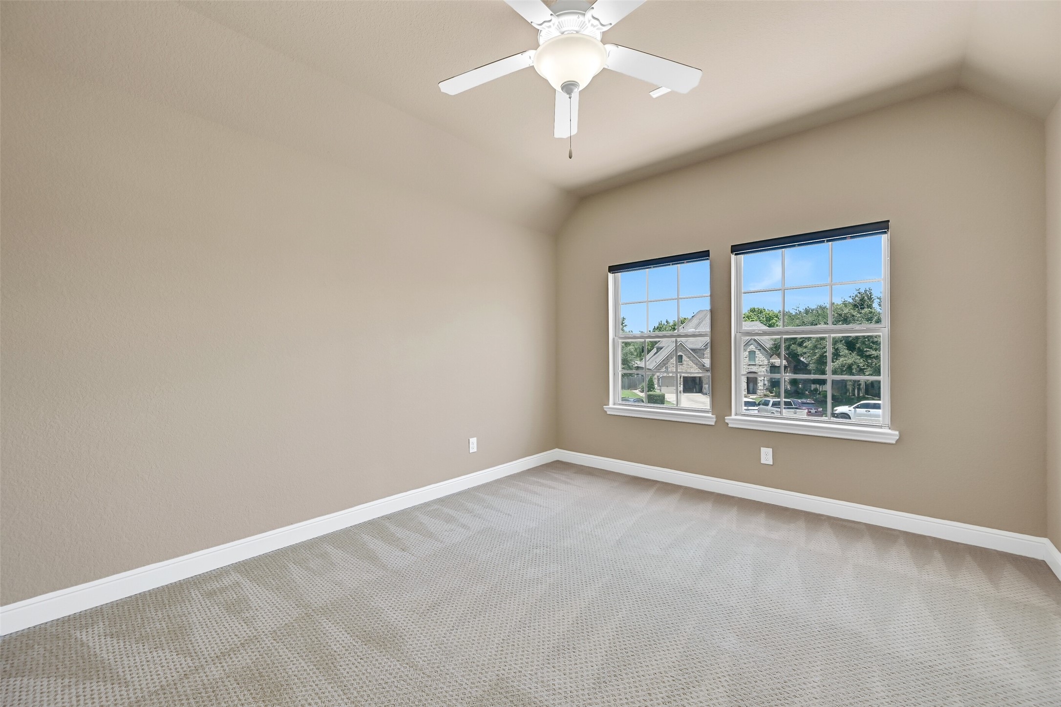Another upstairs secondary bedroom offers raised gambrel ceilings with a lighted ceiling fan, plush sculpted carpet, and large front-facing windows overlooking the neighborhood, creating a welcoming space for family or guests.