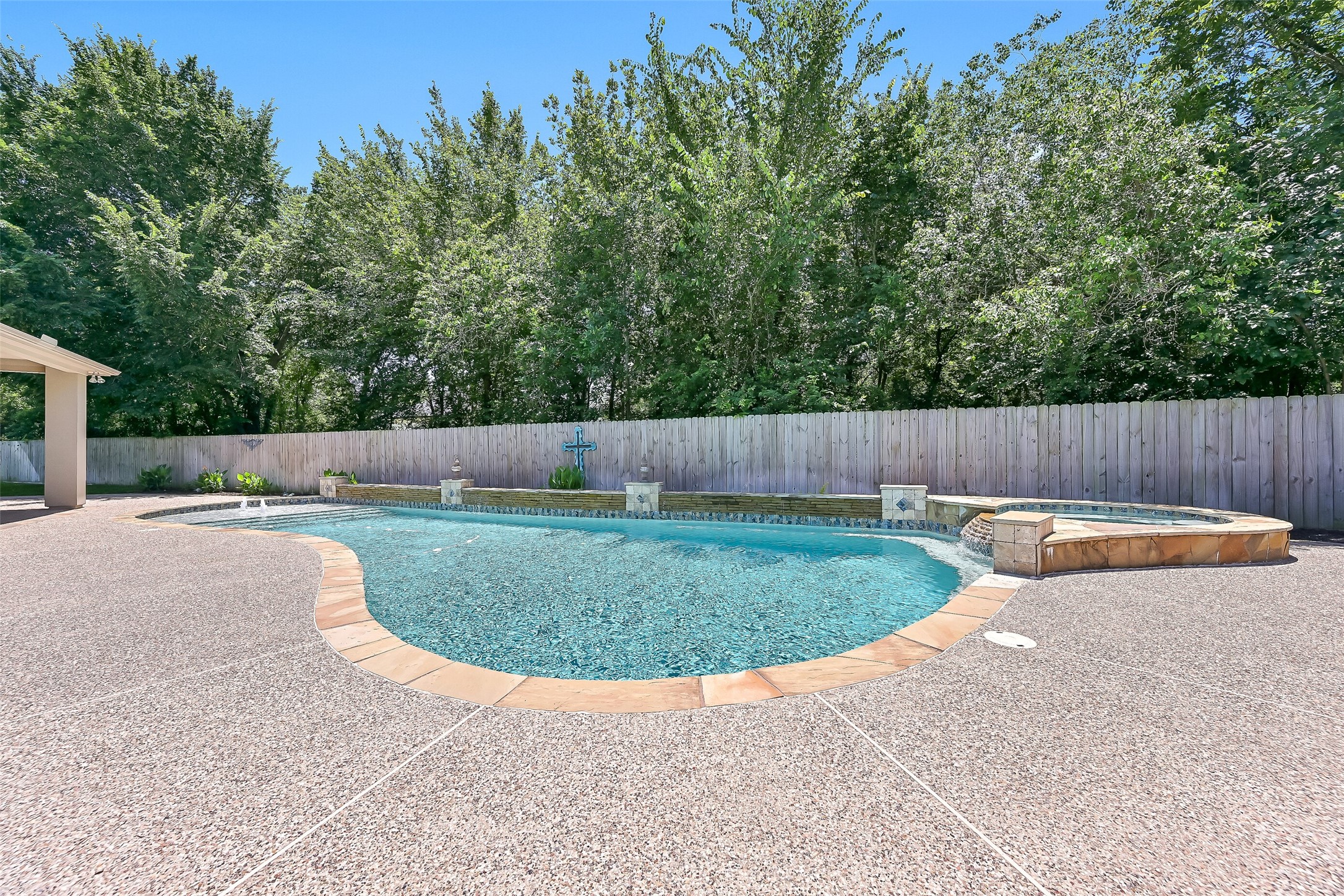 Another view highlights the expansive freeform pool, raised spa, textured decking, and serene wooded backdrop that adds exceptional privacy and shade to this pie-shaped backyard.