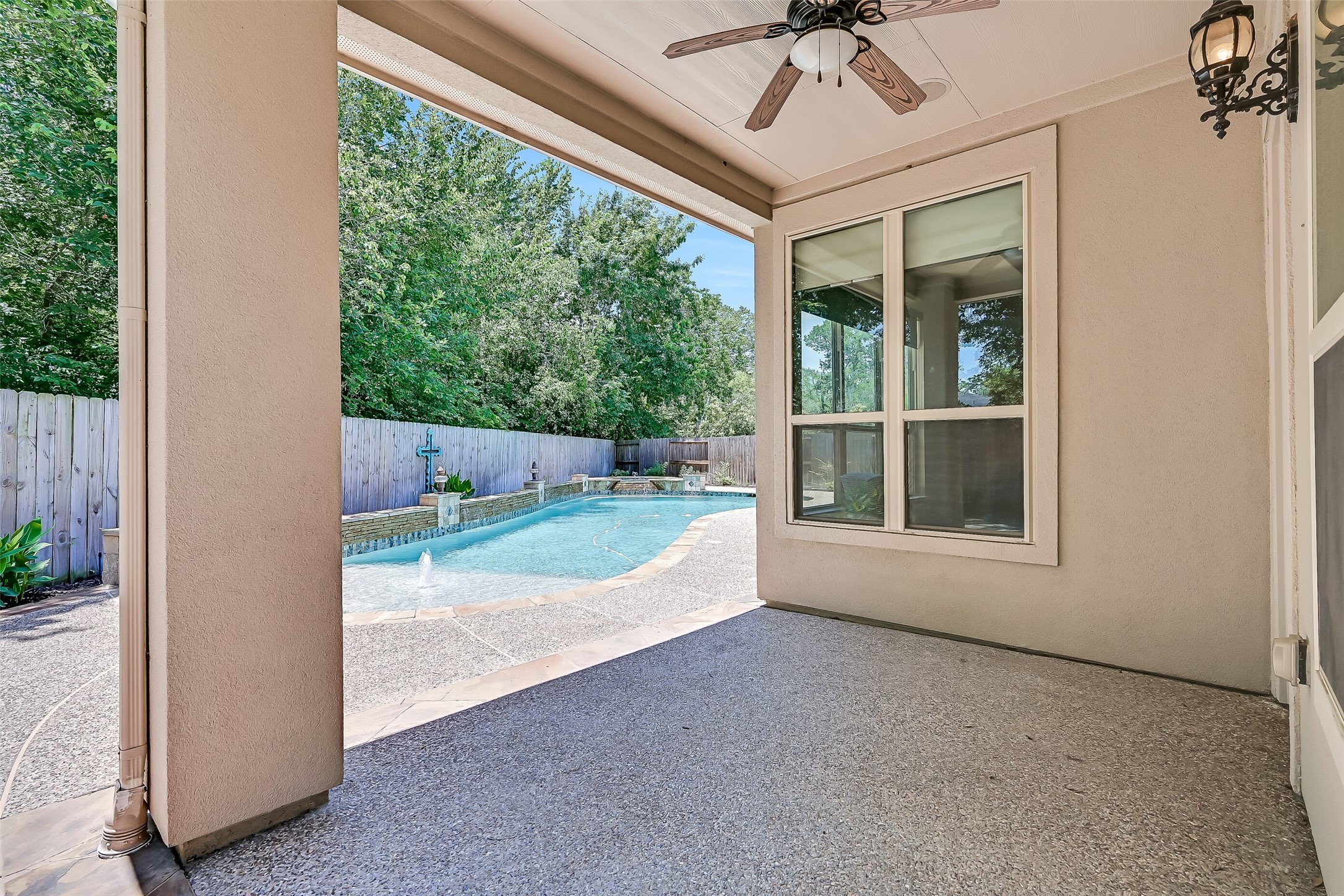 The covered back patio creates a comfortable outdoor living space with a ceiling fan, recessed lighting, built-in speakers, and peaceful views overlooking the resort-style pool and private backyard retreat.