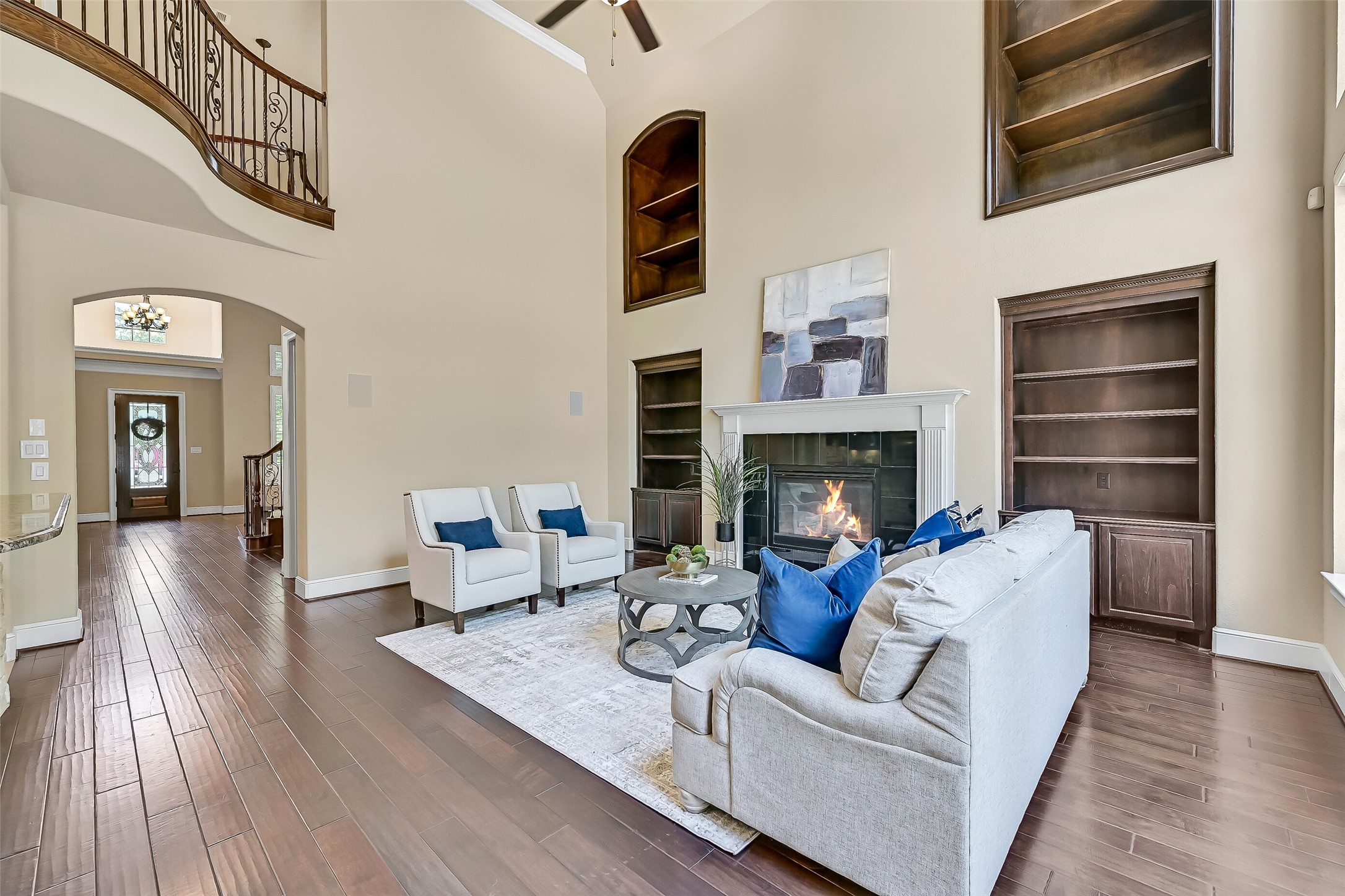The family room makes an unforgettable first impression with 20-foot ceilings, rich engineered wood floors, dramatic floor-to-ceiling windows, and custom built-in shelving stretching toward the second story. A grand gas fireplace with granite tile surround and a milled wood mantle anchors the space while backyard views pour in from every angle.