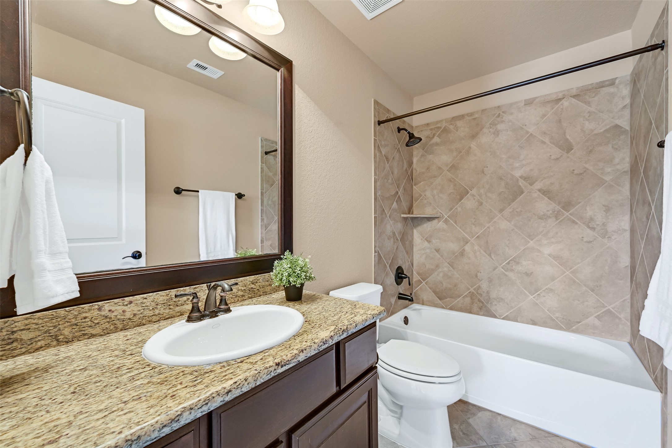 This en suite bathroom continues the homes consistent high-end finishes with granite counters, a single basin sink with oil rubbed bronze faucet, dark espresso stained cabinetry, tile flooring, and a tiled tub/shower combination.