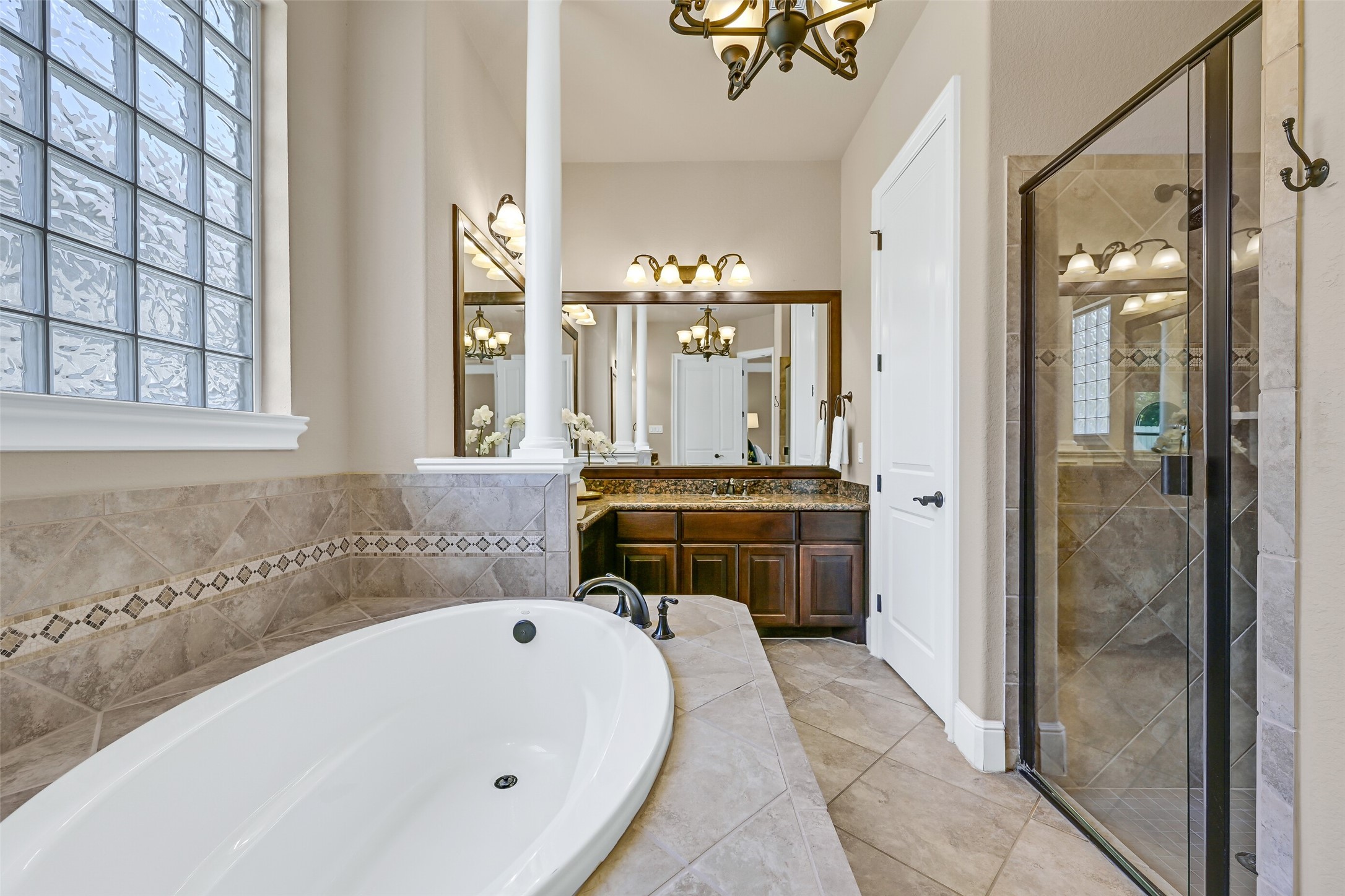 Another angle of the primary bath highlights the oversized soaking tub, glass-enclosed shower with tile surround, framed mirrors, and the thoughtful split-vanity layout that allows the space to function beautifully for everyday routines.