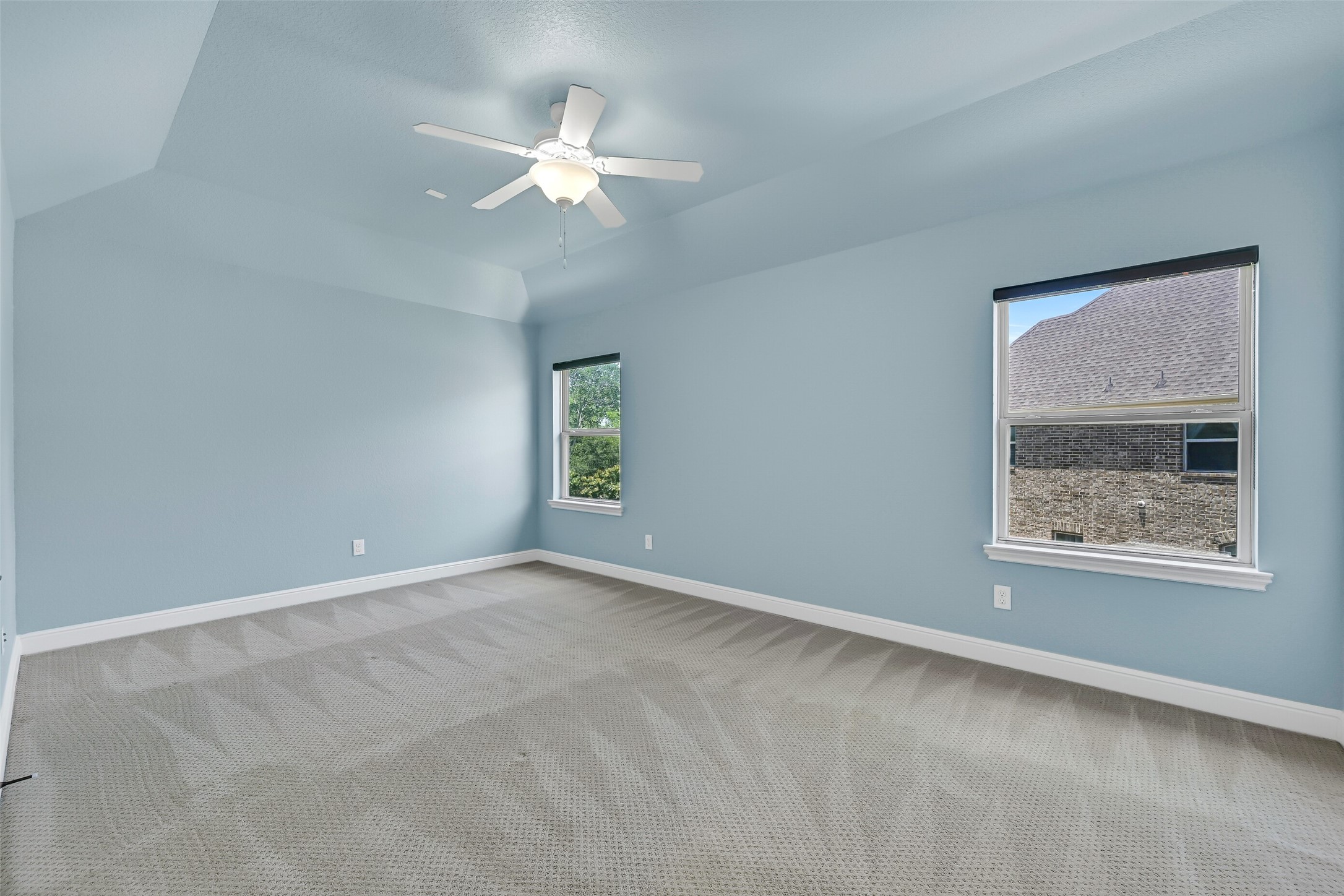 Soft blue walls andelevated gambrel ceilings give this secondary bedroom a bright, calming feel, while generous proportions provide plenty of space for larger furniture or a flexible study setup. A pair of side facing windows bring in natural light.