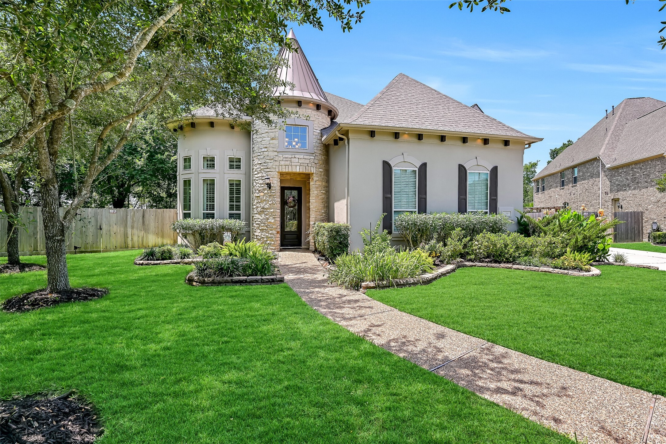A curved walkway winds through lush landscaping to the impressive leaded glass front door, framed by stacked stone detailing and soaring turret architecture. Even before stepping inside, the combination of manicured greenery, custom exterior finishes, and stately design hints at the grand spaces waiting beyond the entry.