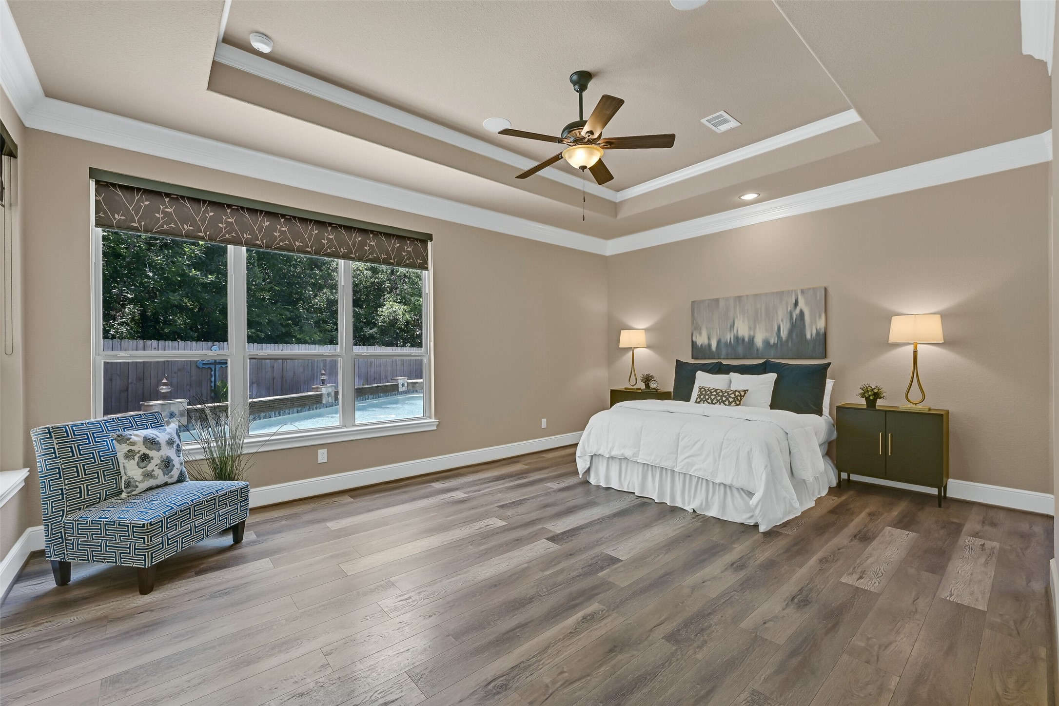 Tucked privately on the first floor, the owners retreat feels like a true sanctuary with a tray ceiling, crown molding, built-in speakers, luxury vinyl plank flooring, and large windows overlooking the pool and backyard. Custom shades and the generous room size create a calm, comfortable atmosphere with plenty of space to unwind.