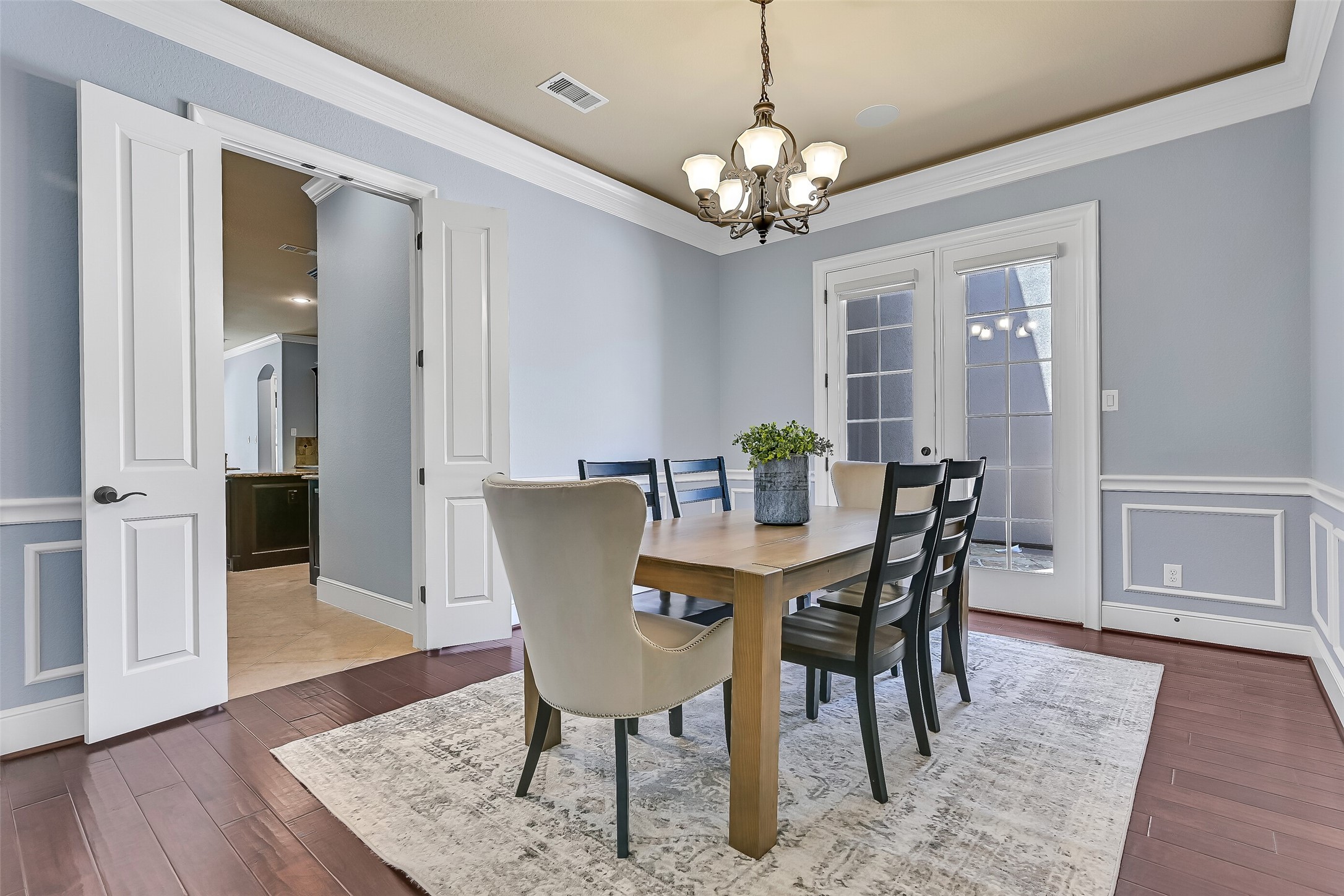 Another view of the formal dining room showcases the detailed millwork, rich wood flooring, and direct access to the butlers pantry and kitchen beyond, while the courtyard-facing French doors allow natural light to pour into the space throughout the day.
