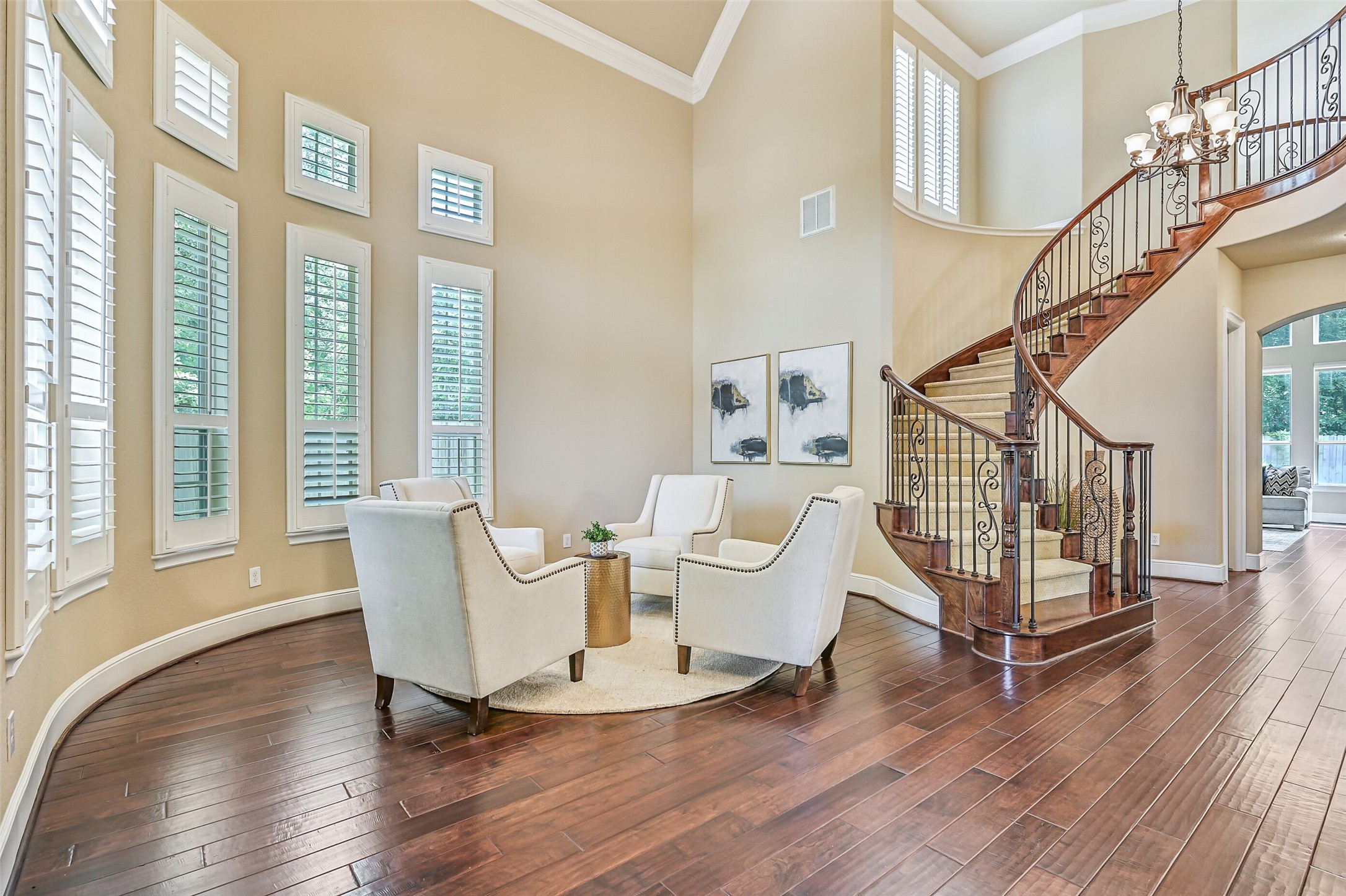 The sweeping staircase becomes a true focal point of the entry with sculpted carpet treads, richly stained woodwork, and intricate iron detailing, all framed by 20-foot ceilings and oversized windows that create an airy, open feel from the moment you walk in.