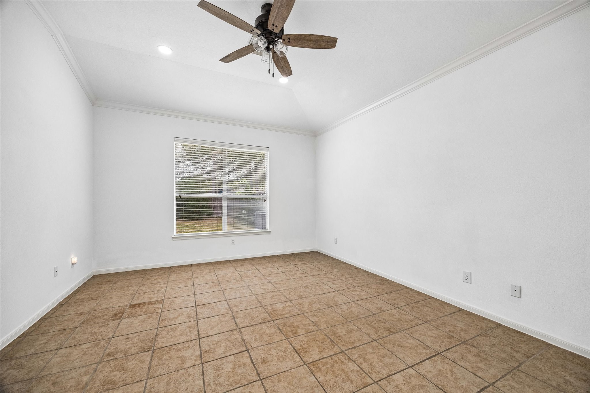 Spacious primary bedroom with vaulted ceilings, neutral tile flooring, and a large window offering natural light and a view of the backyard.