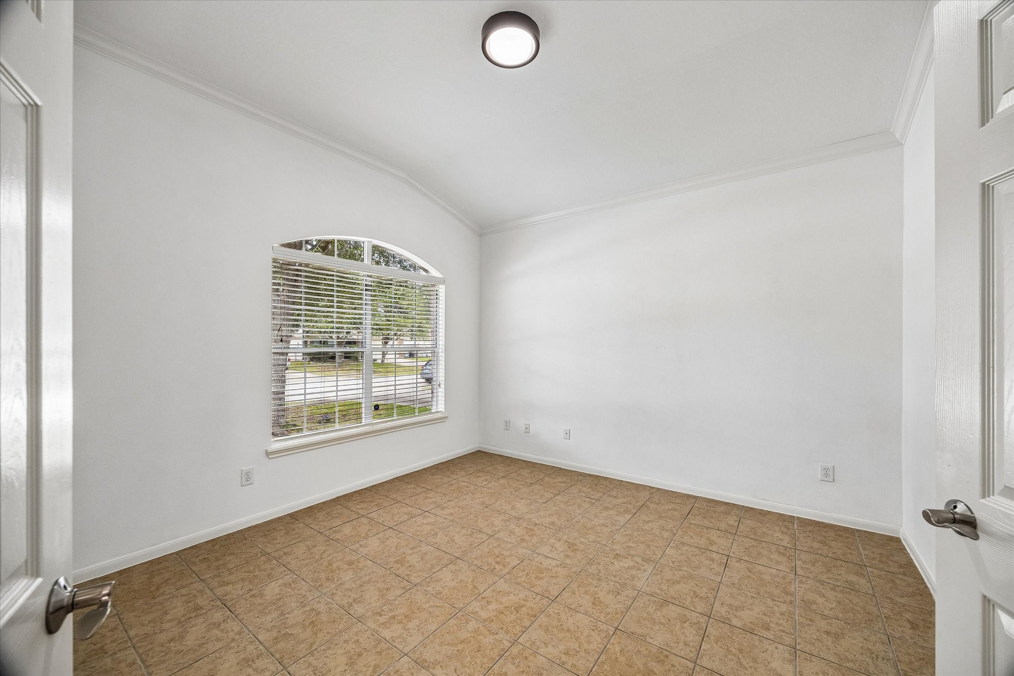 Bright and inviting room with large arched window, neutral tile flooring, and crisp white walls, perfect for a cozy study or home office.