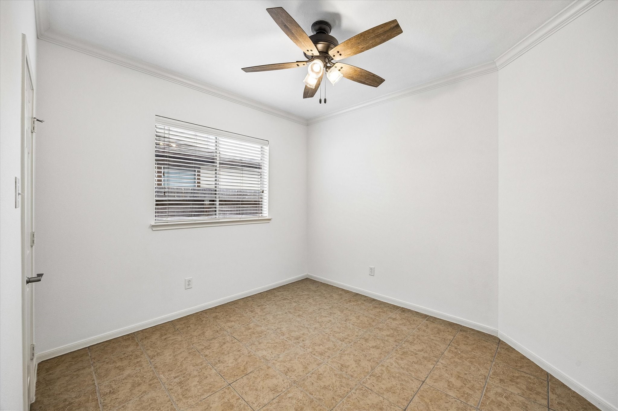 Bright and airy second guest bedroom featuring neutral tile flooring, a ceiling fan with lights, and a window with blinds, perfect for versatile use.