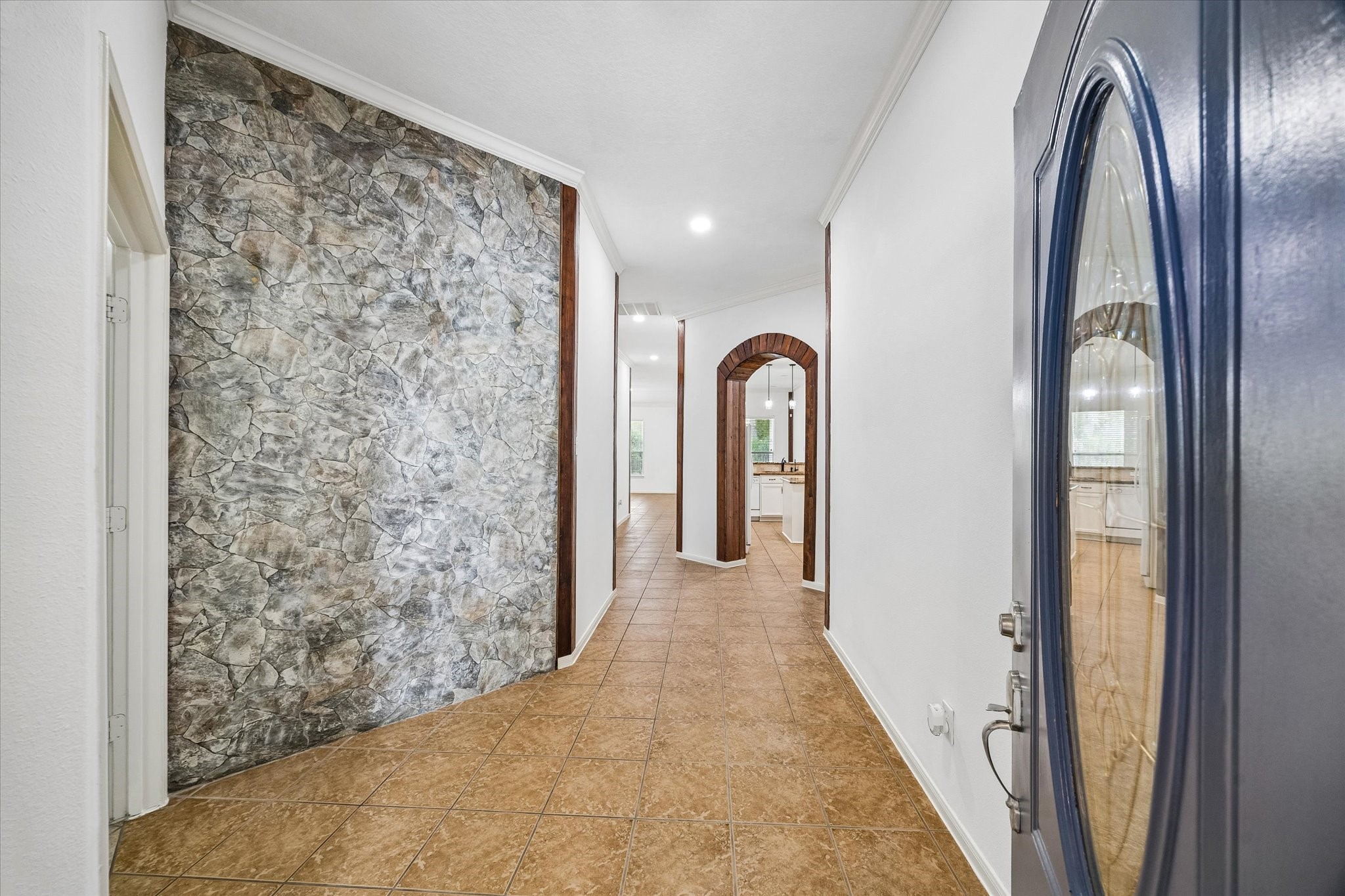 Inviting entryway with a unique stone-accented wall, warm tile flooring, and elegant archways leading to an open living space.