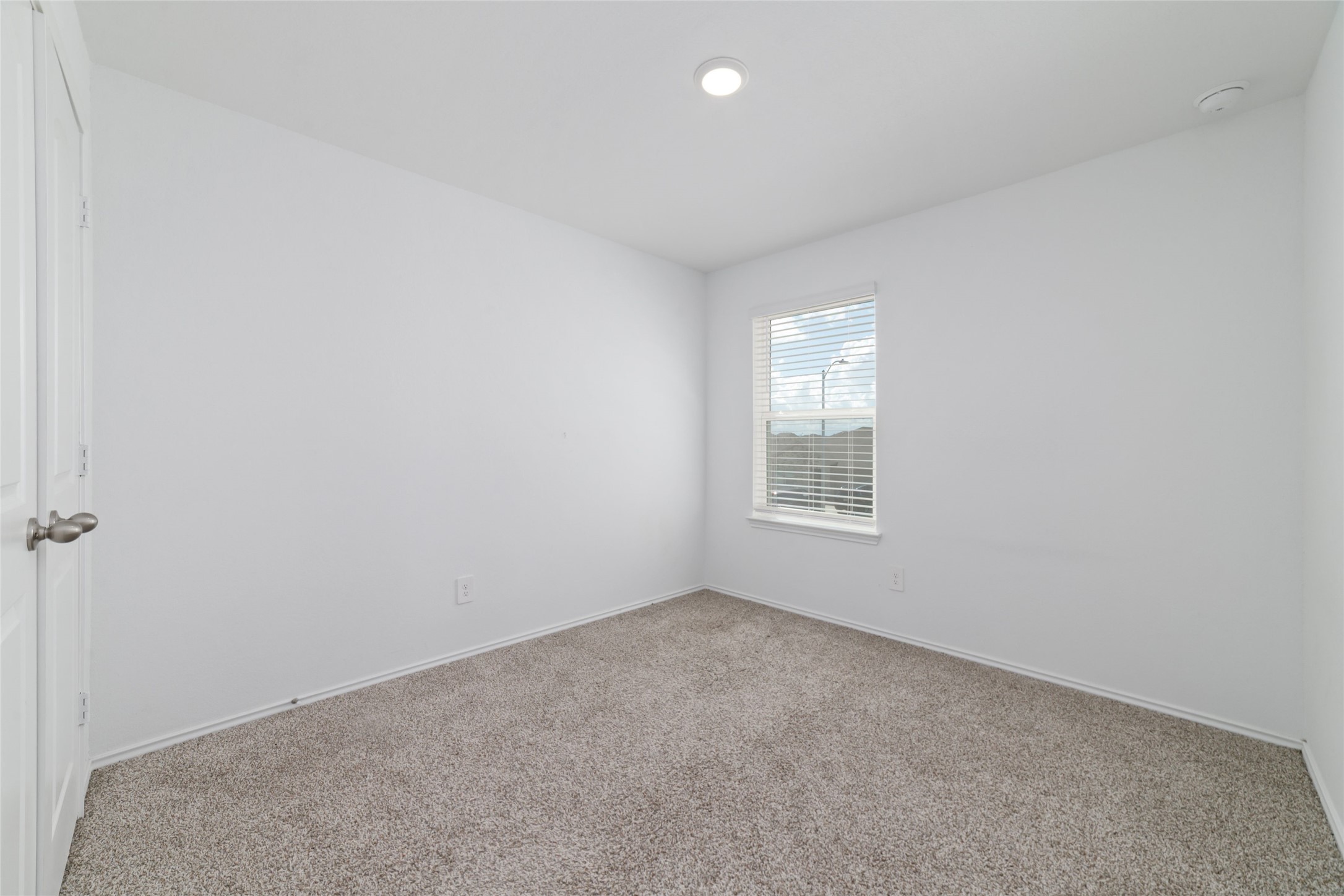 (Upstairs Bedroom 3): Generously sized secondary bedroom located on the second floor, featuring soft neutral carpeting, crisp white walls, and a recessed ceiling light. A large, front-facing window fitted with custom blinds fills the room with abundant natural light, making it a bright, comfortable space ideal for a children's bedroom, guest room, or dedicated home office